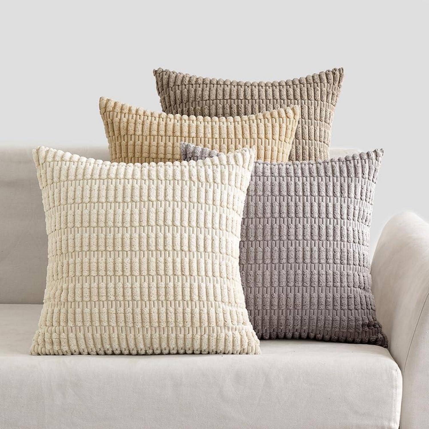 Drei strukturierte Zierkissen in neutralen Farbtönen sind ordentlich auf einem beigen Sofa drapiert und verleihen der Einrichtung eine gemütliche und stilvolle Note.