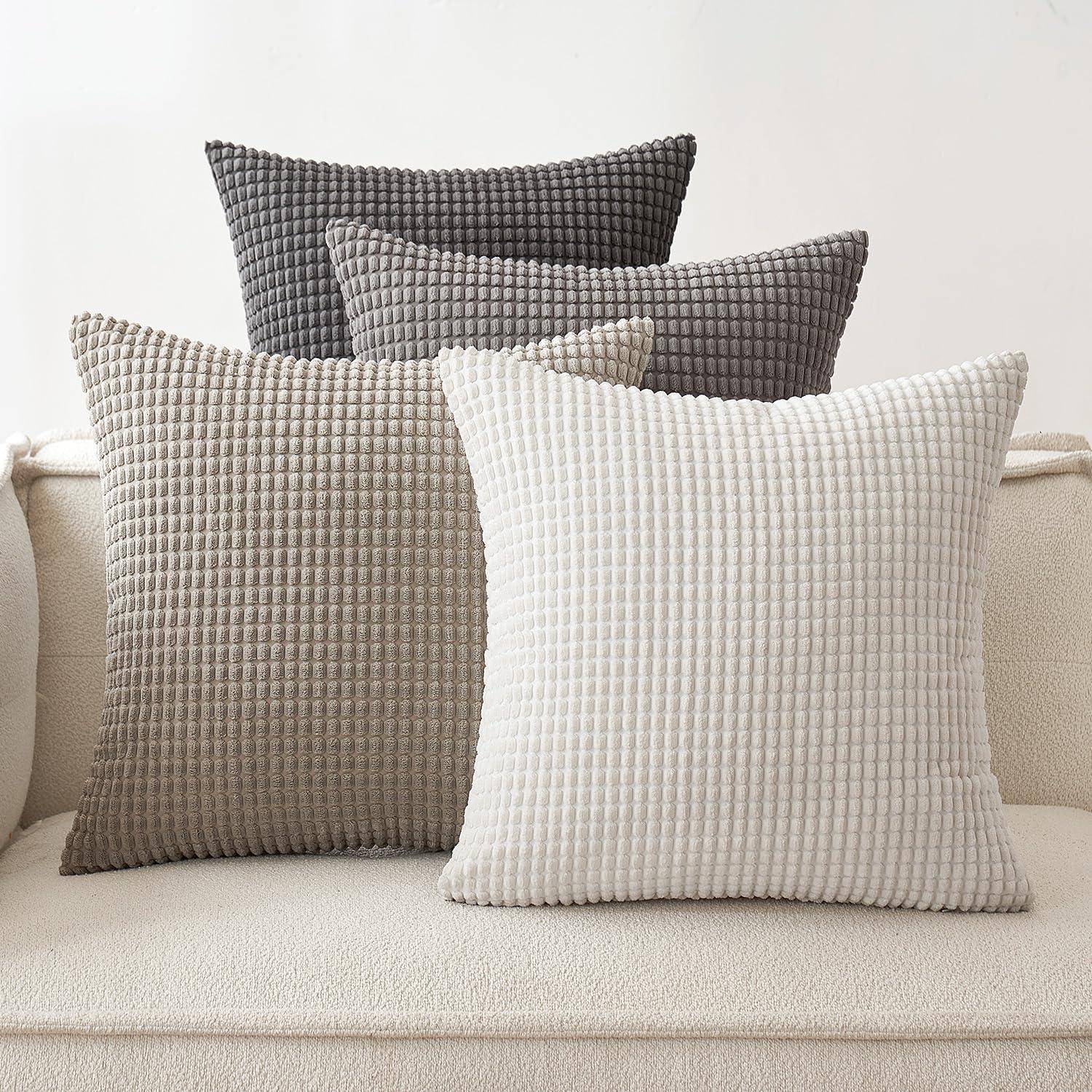 Vier strukturierte Kissen in Nuancen von Creme, Beige und Grau sind ordentlich auf einem beigen Sofa angeordnet und schaffen eine gemütliche, neutrale Atmosphäre.