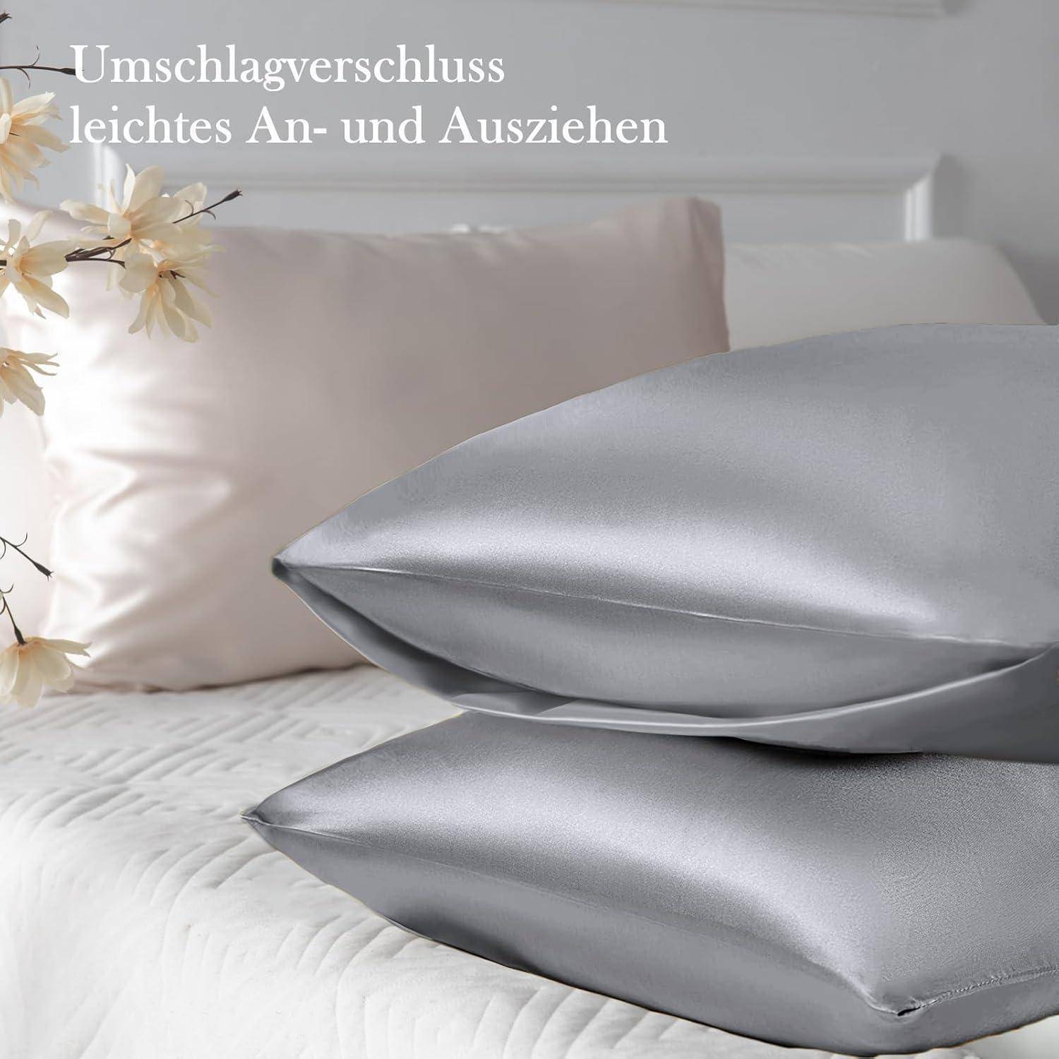 Silberne und rosafarbene Satin-Kissenbezüge auf einem Bett, geschmückt mit weißen Blumen. Im Hintergrund deutscher Text mit dem Hinweis 