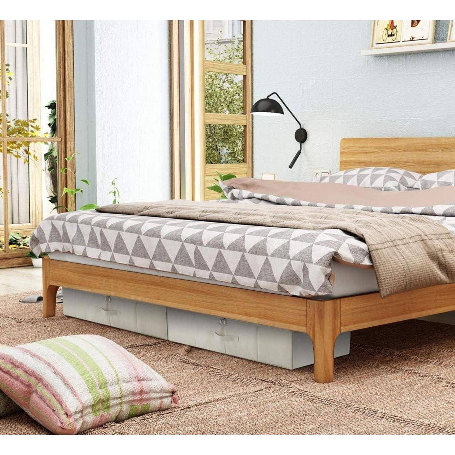 Ein gemütliches Schlafzimmer mit einem Holzbett, das mit grauer, gemusterter Bettwäsche und einem beigen Überwurf ausgestattet ist, Kissen auf dem Holzfußboden und einer Wandlampe.