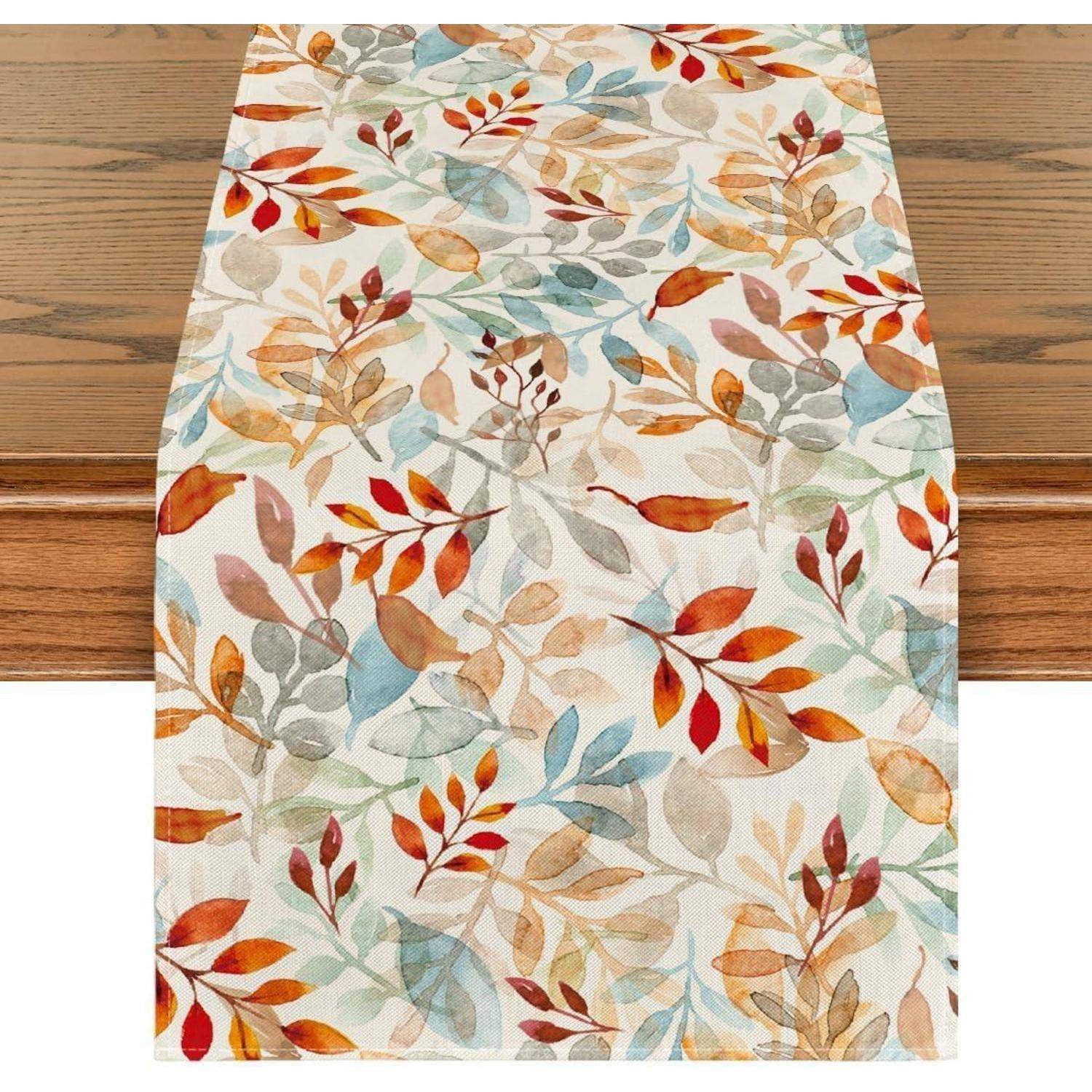 Ein Tischläufer mit einem Herbstblättermuster in Schattierungen von Orange, Rot, Braun und Blau auf einem Holztisch.