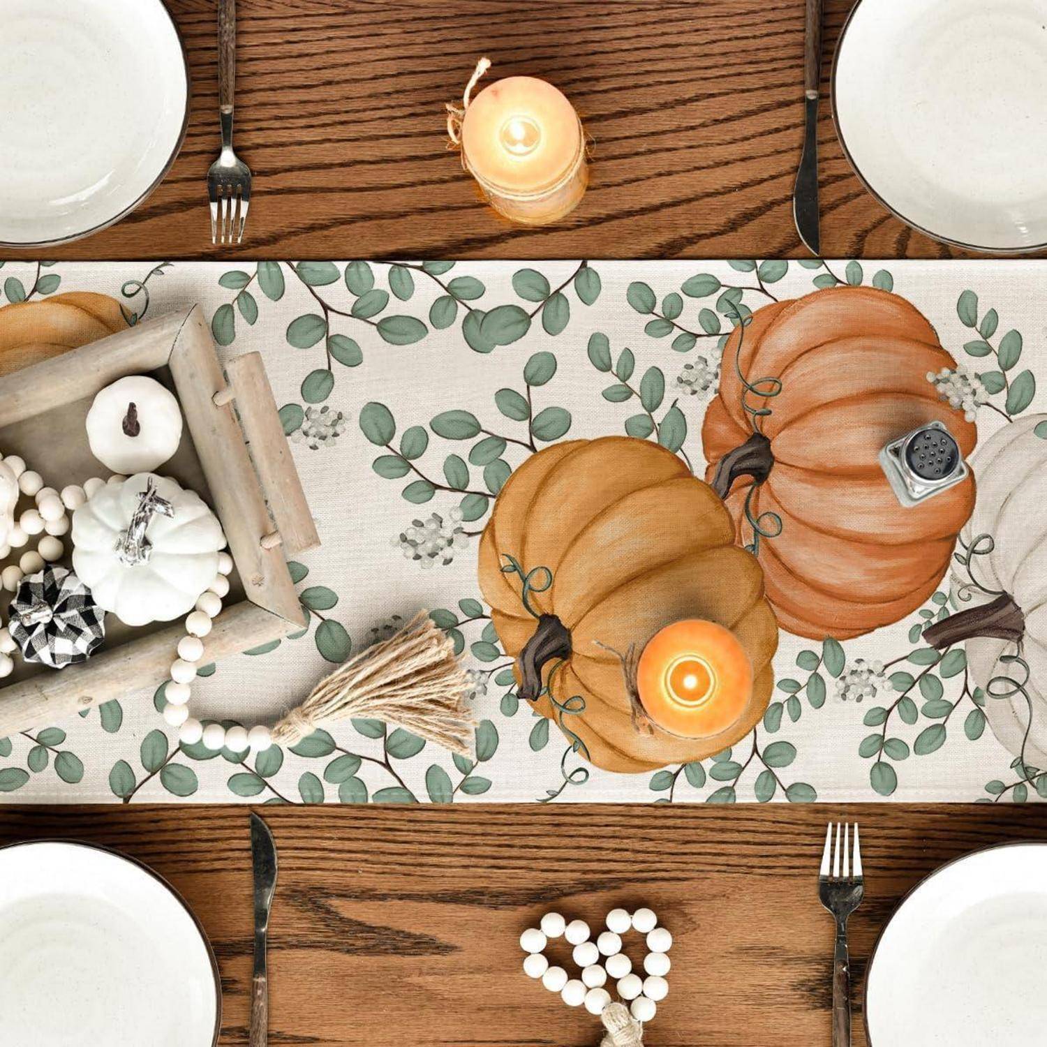 Herbstlich gestaltete Tischdekoration mit Kürbissen, Kerzen und dekorativen Perlen auf einem Holztisch, umgeben von Tellern und Besteck.