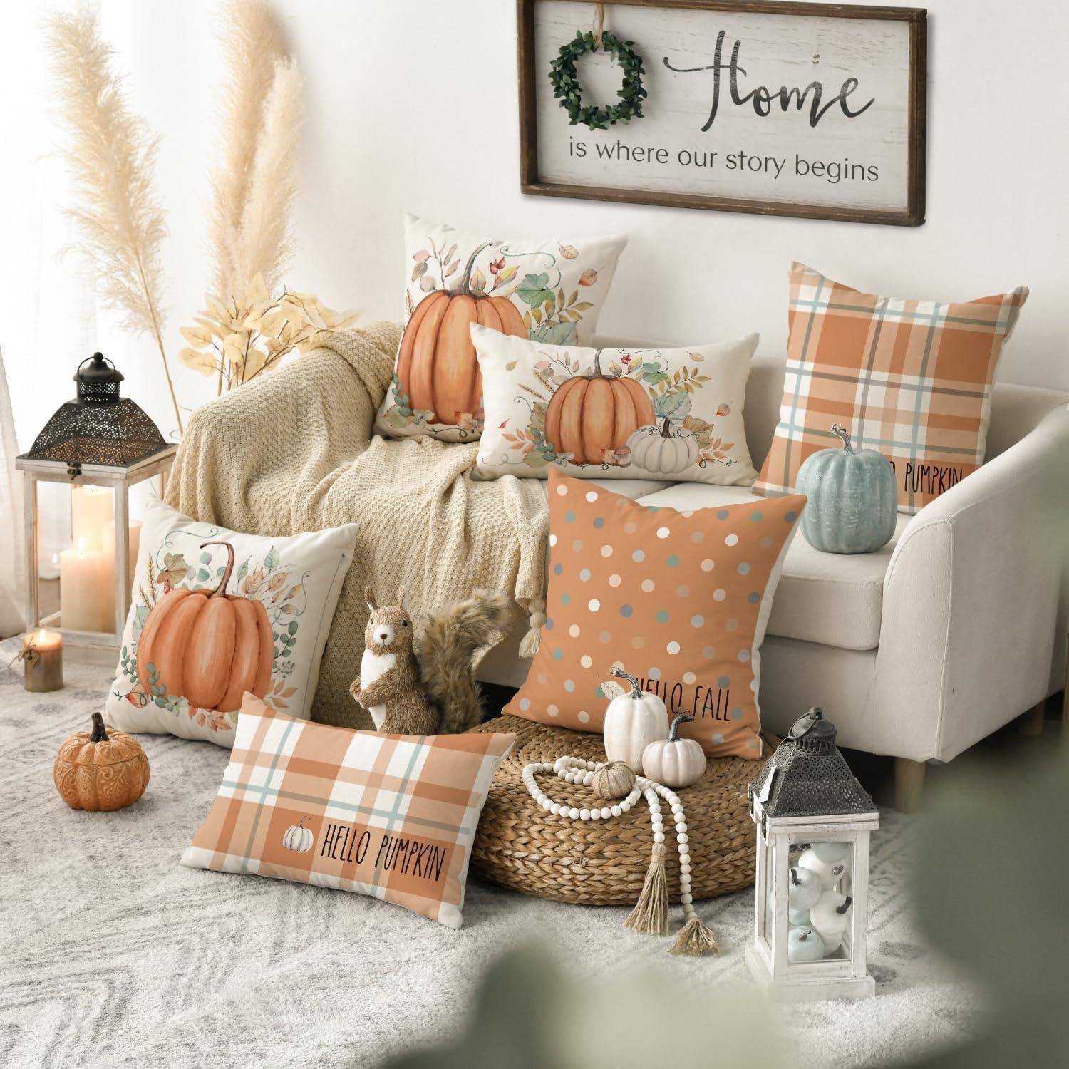 Ein gemütliches Wohnzimmer mit Herbstthema, das Kürbis-Kissen, eine karierte Decke, Laternen und ein Schild mit der Aufschrift „Zuhause ist dort, wo unsere Geschichte beginnt