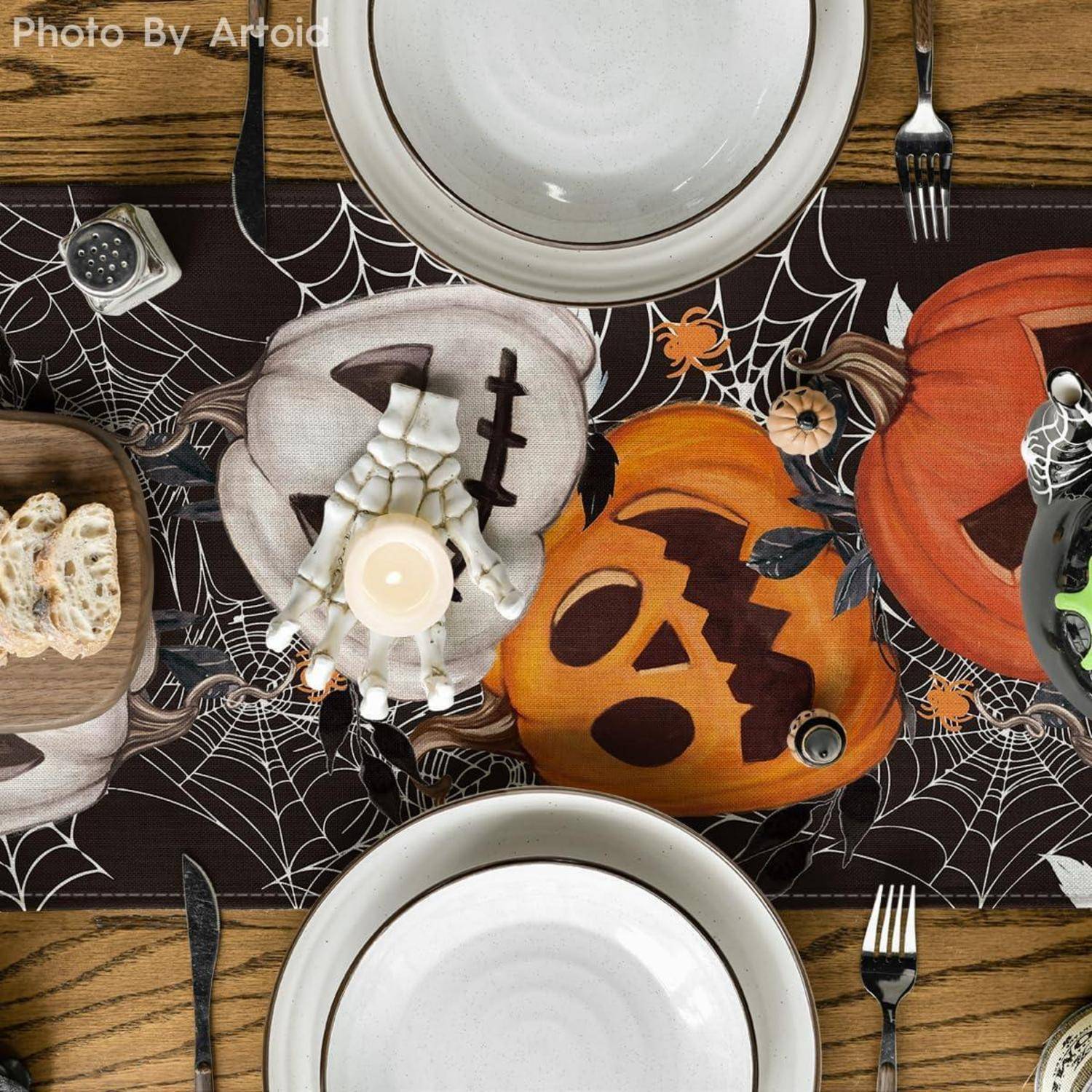 Eine halloweenthematische Tischdecke mit weißen Tellern, Silberbesteck, Brot und Kerzen. Ziert von Kürbisschnitzereien auf einem dunklen Tischläufer.