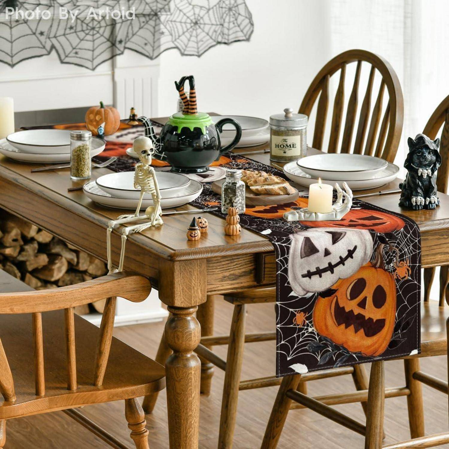 Ein hölzerner Esstisch ist für eine Halloween-thematische Mahlzeit gedeckt mit Tellern, einem Kessel, einem Skelett, Kerzen, Kürbis- und Katzendekorationen.