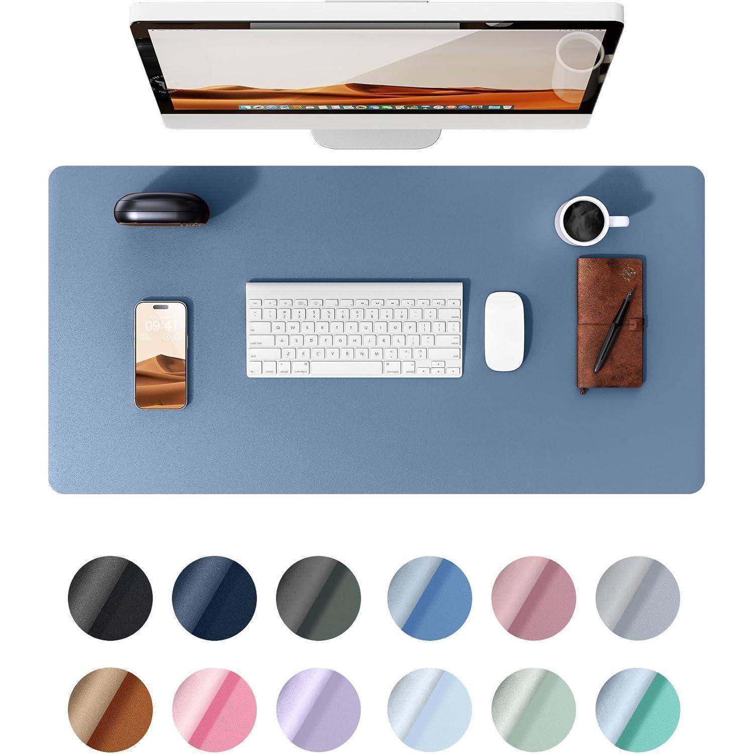 Ein aufgeräumter Schreibtisch mit einem Computer, Tastatur, Maus, Smartphone, Kaffeetasse und Notizbuch auf einer blauen Unterlage, umgeben von Farbmustern.
