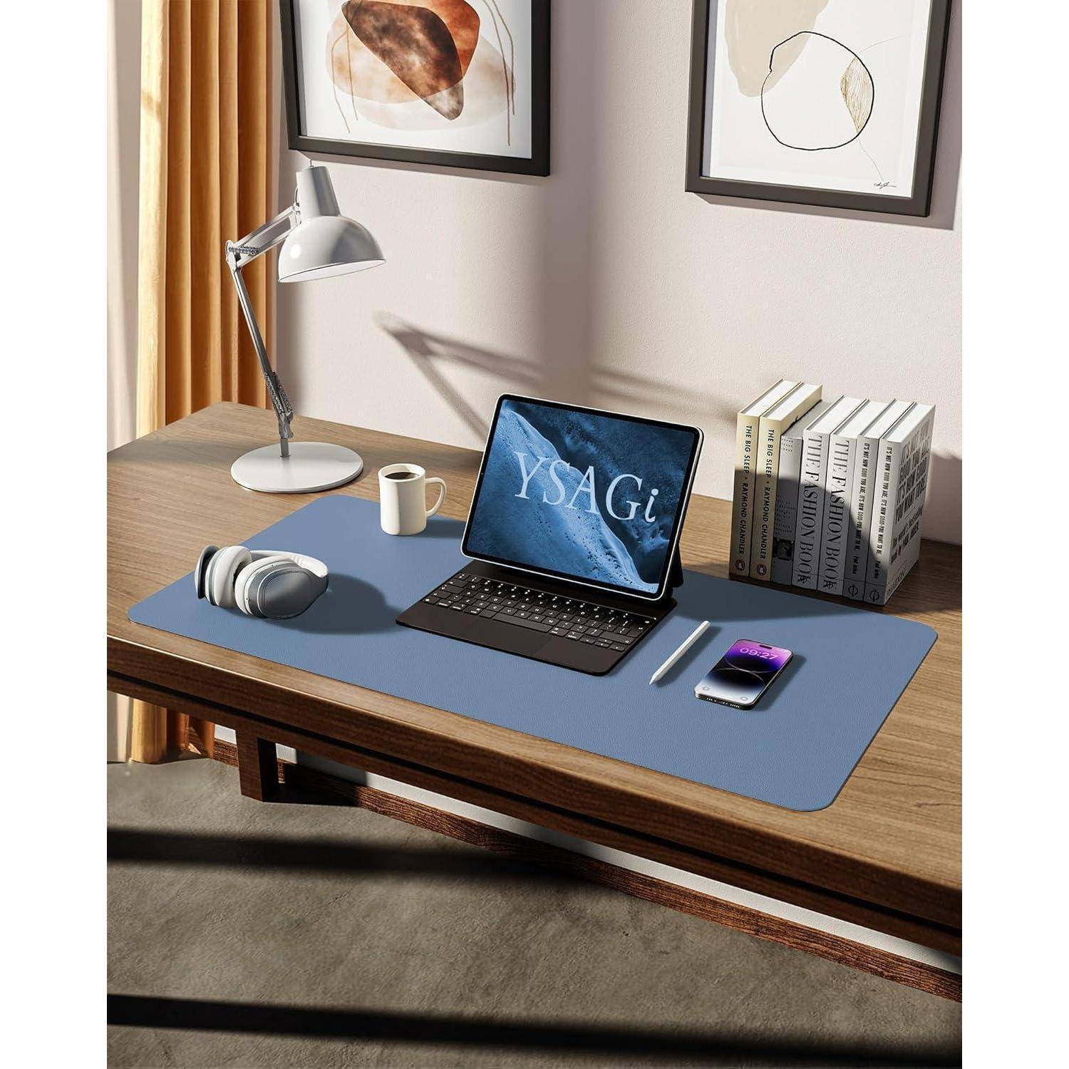 Ein aufgeräumter Arbeitsplatz mit einem Laptop, auf dem 'YSAGi' angezeigt wird, einem Smartphone, Kopfhörern, einer Lampe und Büchern, der auf einem Holzschreibtisch steht, mit Kunst an der Wand.