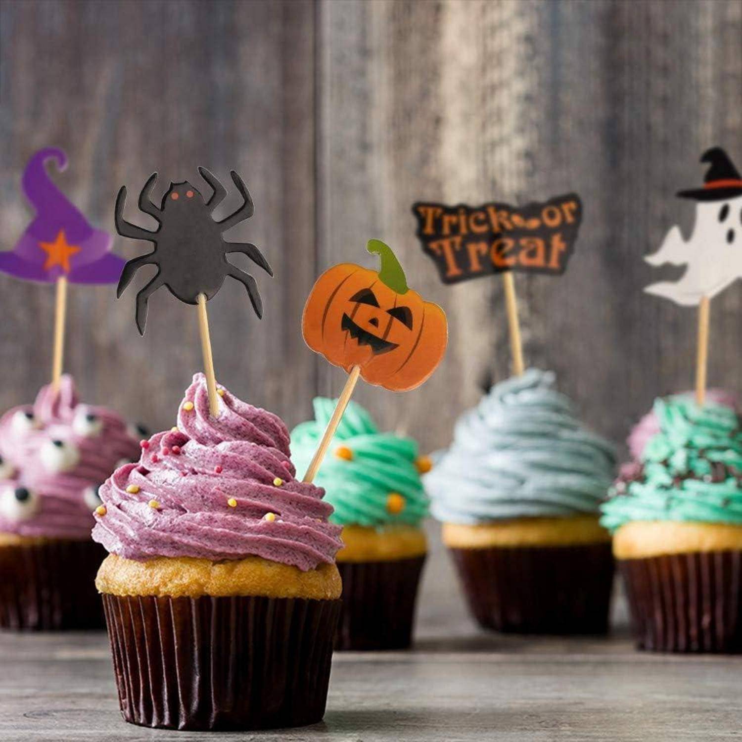 Bunte Cupcakes mit Halloween-Motiven: ein Hexenhut, Spinne, Kürbis, Geist und ein 