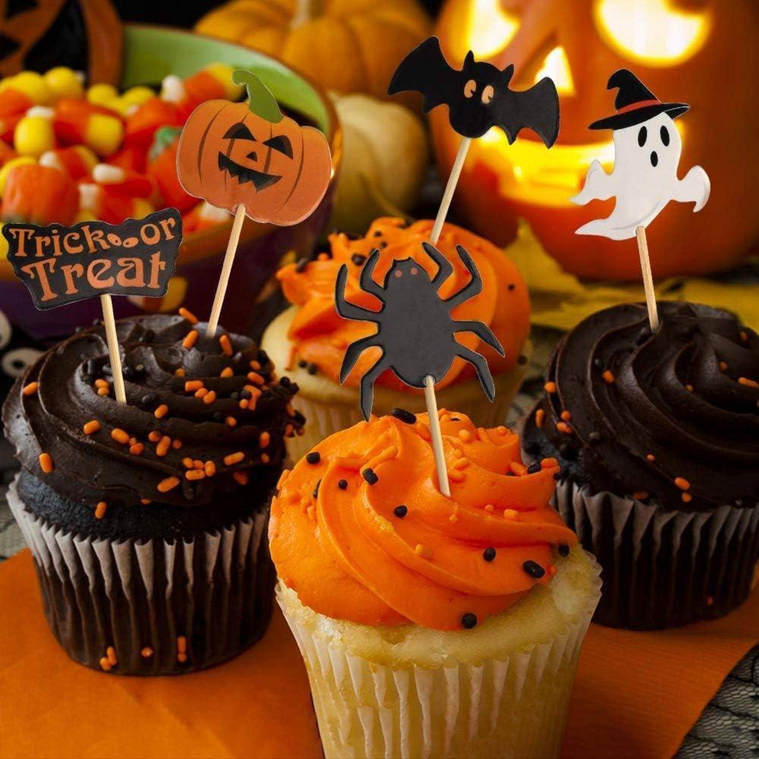 Cupcakes mit orange und schwarzer Buttercreme, verziert mit Halloween-Motiven wie Kürbis, Fledermaus, Spinne und Geist, umgeben von Süßigkeiten.