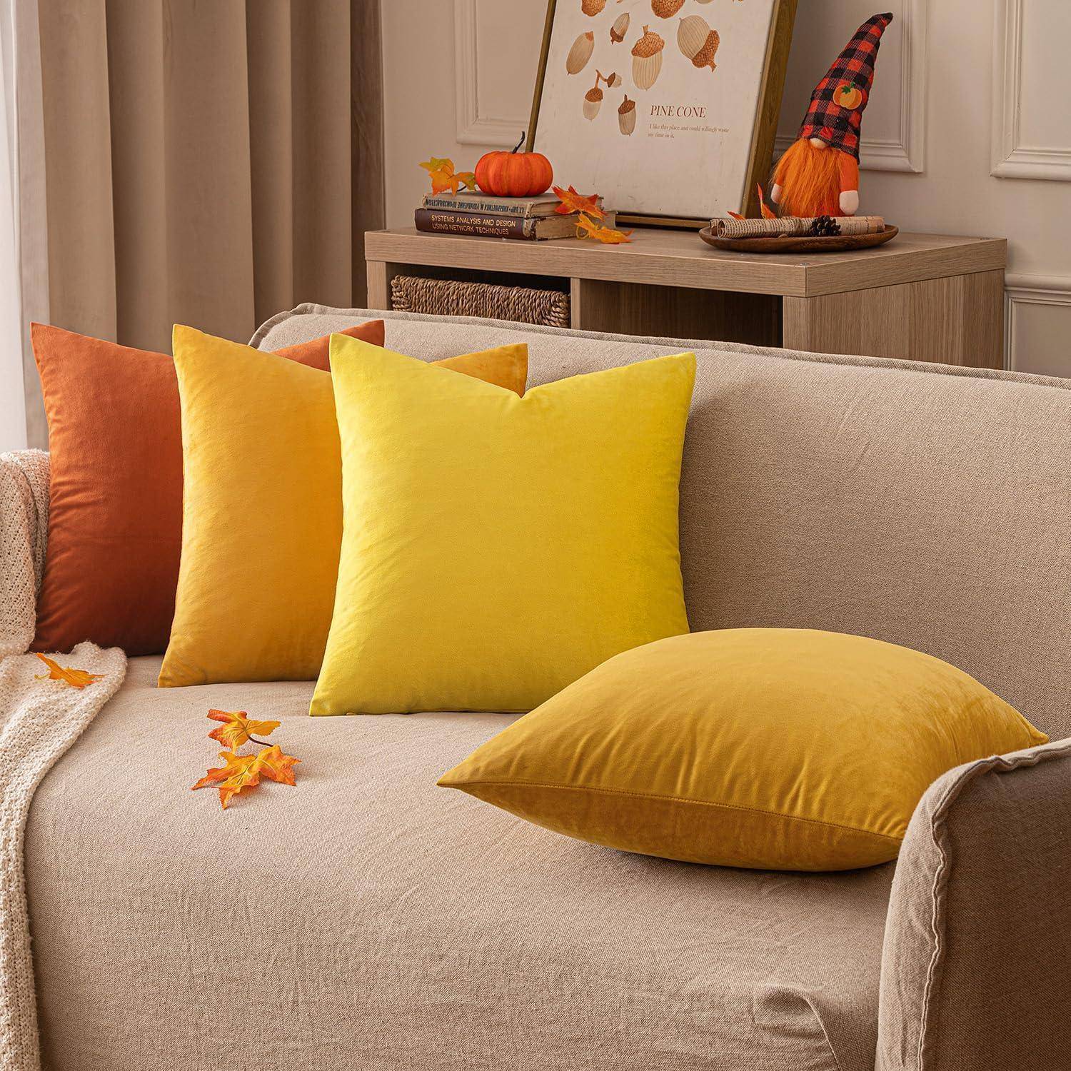 Ein gemütliches Wohnzimmer mit Herbstthema, ausgestattet mit einem beigen Sofa, lebhaften gelben und orangefarbenen Kissen und dekorativen Kürbissen auf einem Regal.