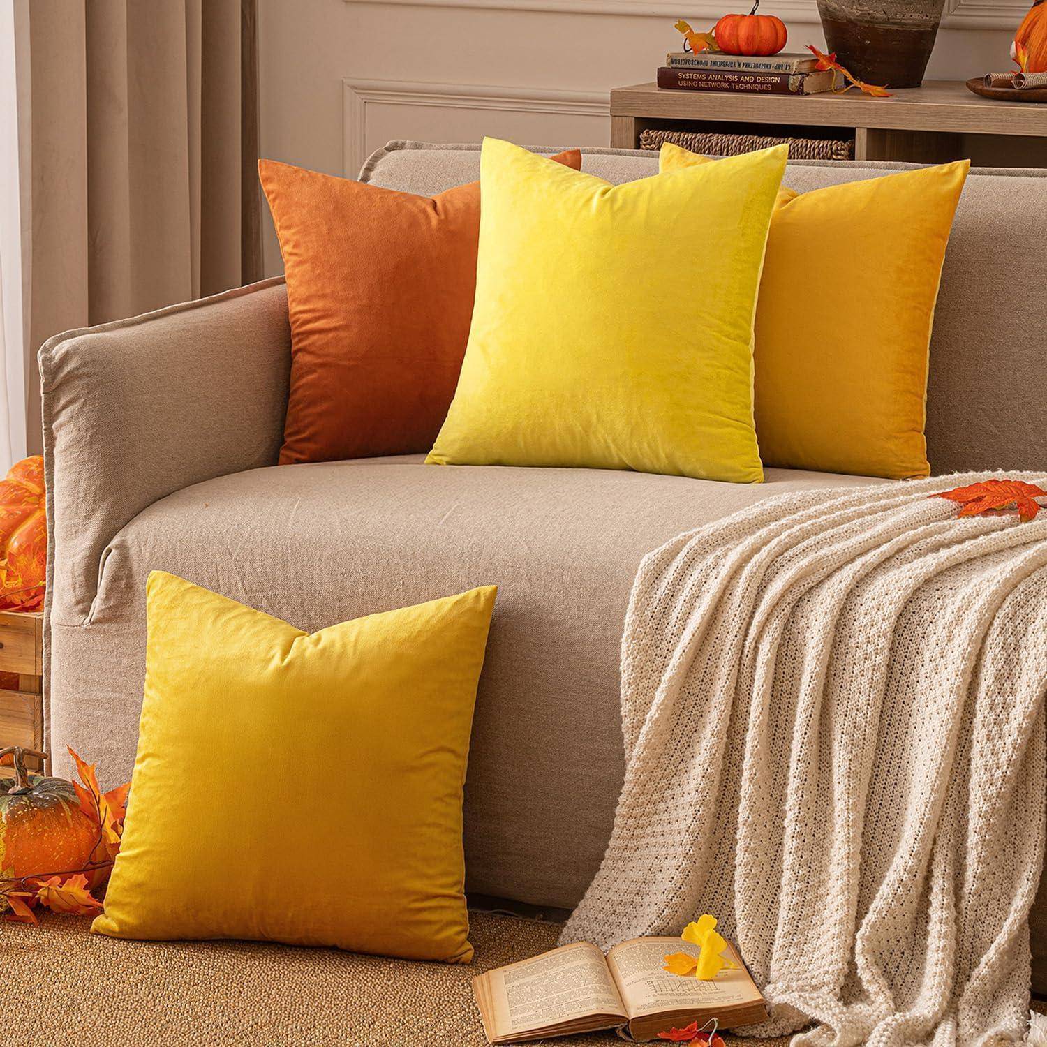 Ein beiges Sofa mit lebhaft gelben und orangen Kissen, umgeben von Herbstdekoration wie Kürbissen und herabgefallenen Blättern, die eine gemütliche Atmosphäre schaffen.