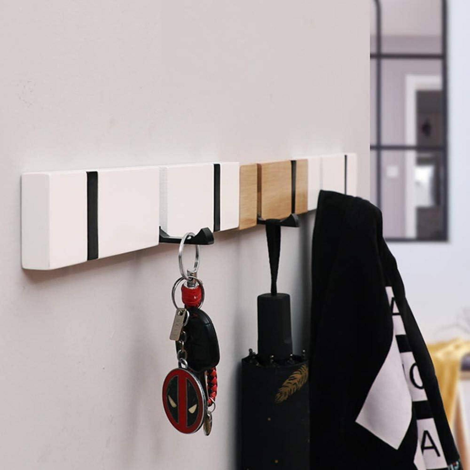 Eine an der Wand montierte weiße und holzfarbene Garderobe hängt Schlüssel mit einem Charakterschlüsselanhänger und einer schwarzen Tasche, in einem modernen Raum mit unscharfem Hintergrund.
