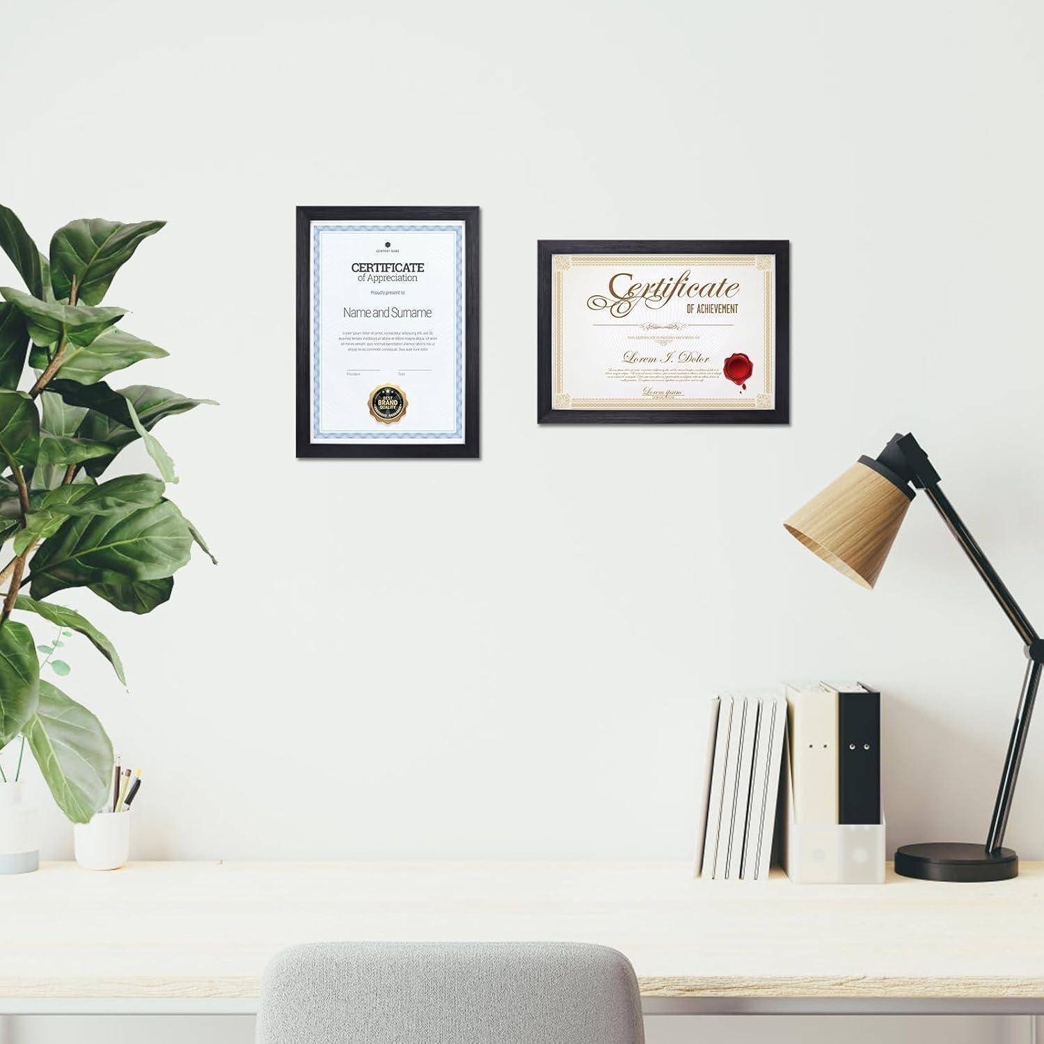 Zwei gerahmte Zertifikate hängen an einer weißen Wand über einem Schreibtisch mit einer Lampe, Büchern und einer Pflanze und schaffen so ein professionelles Büroambiente.