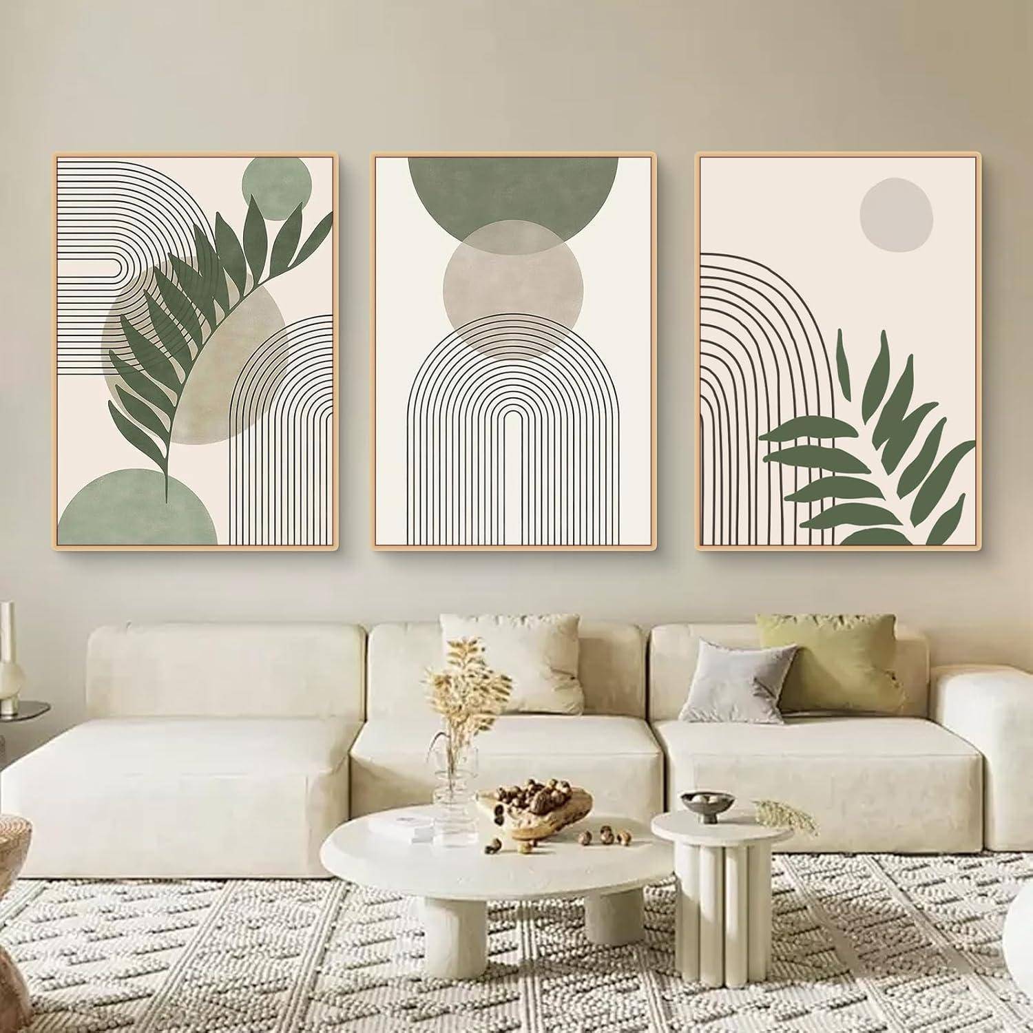 Ein moderner Wohnraum zeigt ein weißes Sofa und einen runden Couchtisch. Drei abstrakte Kunstwerke mit geometrischen Formen und Blättern hängen darüber.