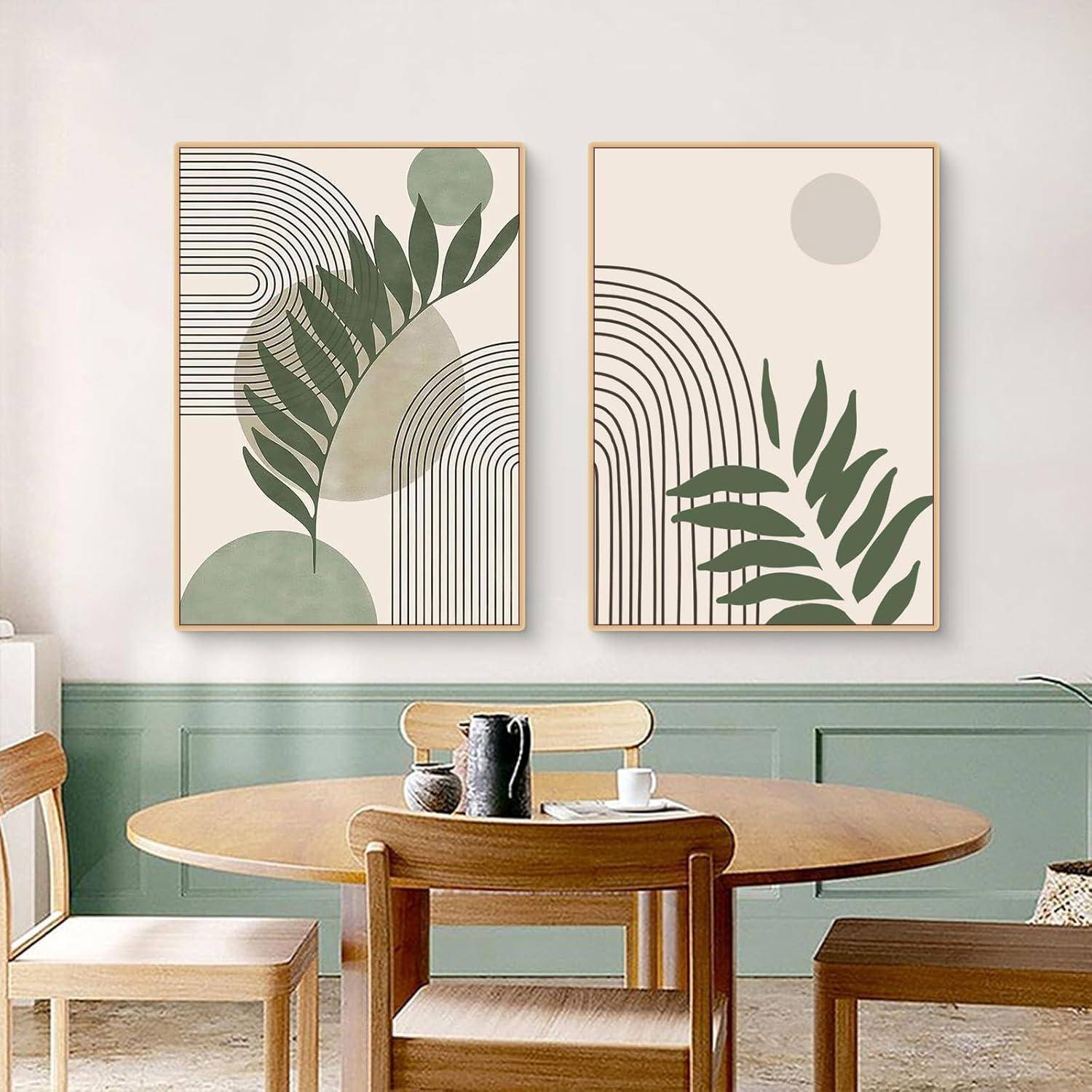 Zwei abstrakte Kunstwerke mit grünen Blättern und geometrischen Formen hängen über einem Holztisch mit Stühlen in einem gemütlichen Raum.