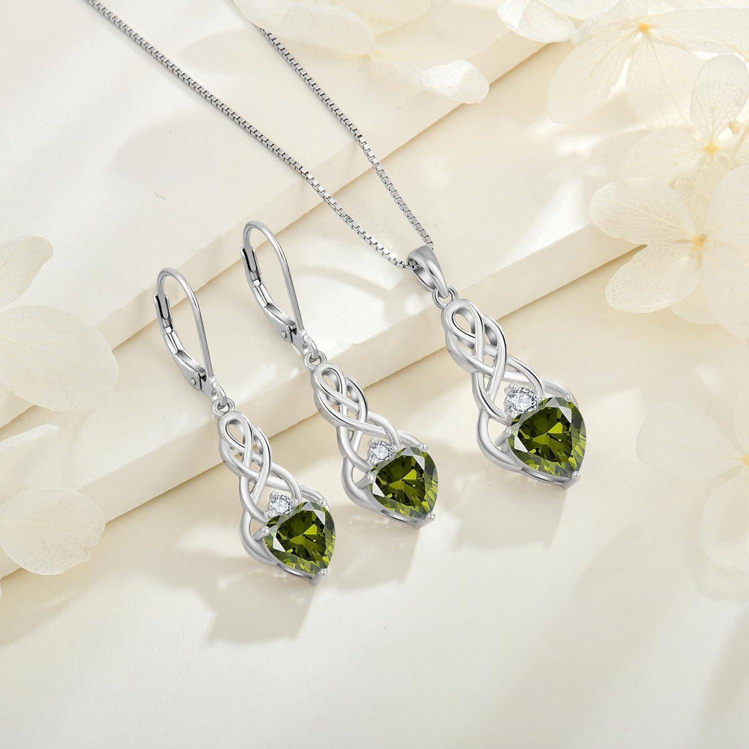 Silberne Halskette und Ohrringe aus Sterlingsilber mit kunstvollen keltischen Knotenmustern, versehen mit grünen tränenförmigen Edelsteinen, vor einem Blumenhintergrund.