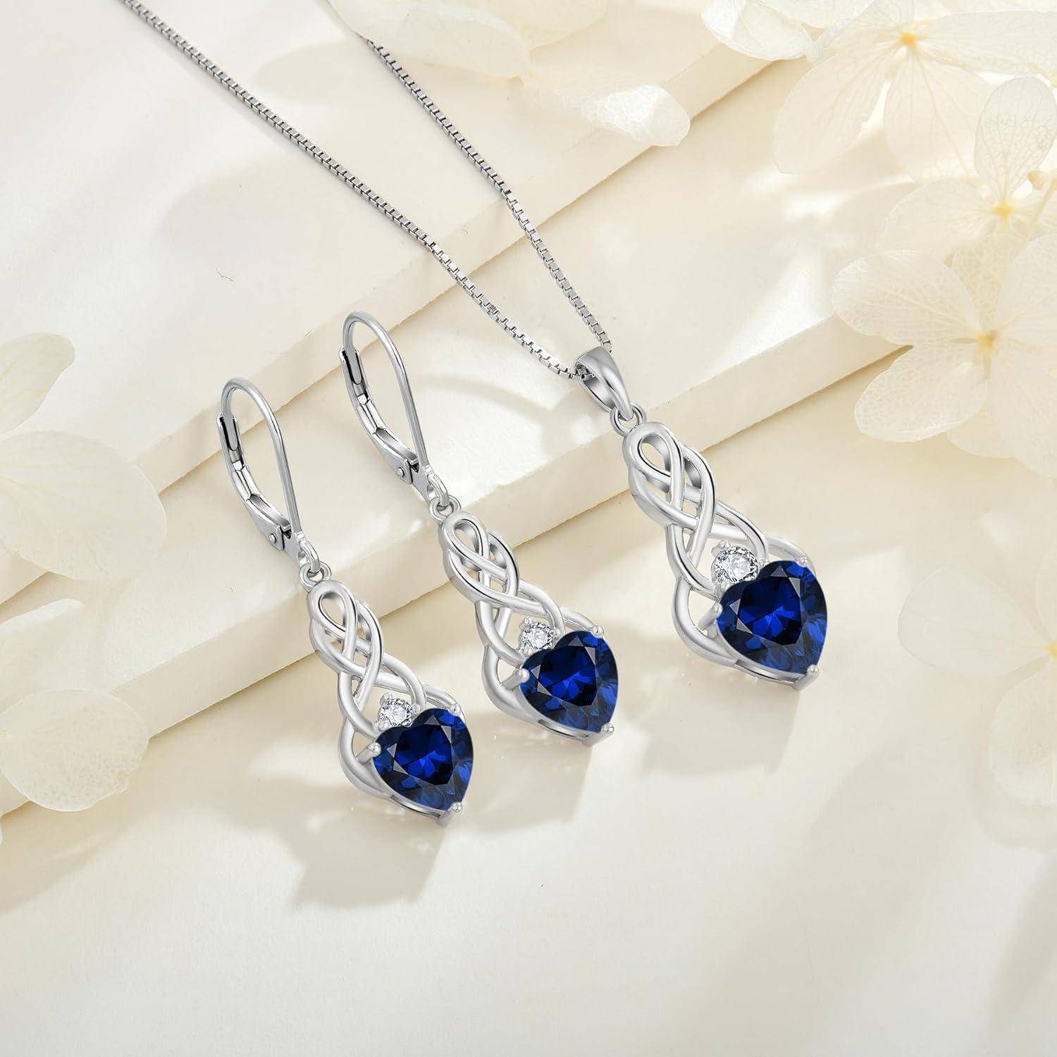 Eine Silber-Halskette und ein Ohrringe-Set mit herzförmigen blauen Edelsteinen, präsentiert auf einem hellen Hintergrund mit sanften Blumenakzenten.