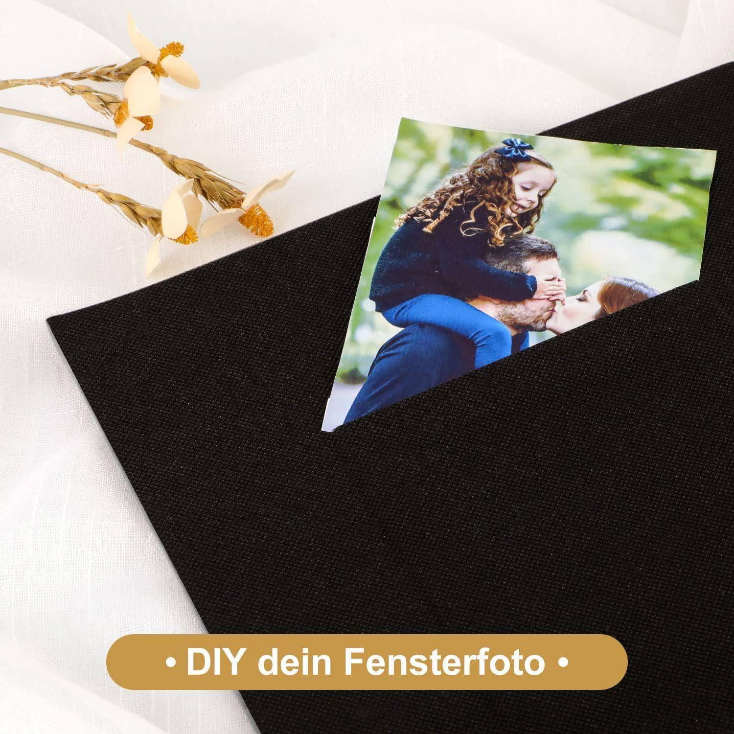 Foto einer lächelnden Frau, die ein Kind in einer Außenumgebung umarmt, auf einer schwarzen Oberfläche platziert mit getrockneten Blumen in der Nähe. Text lautet 'DIY dein Fensterfoto'.