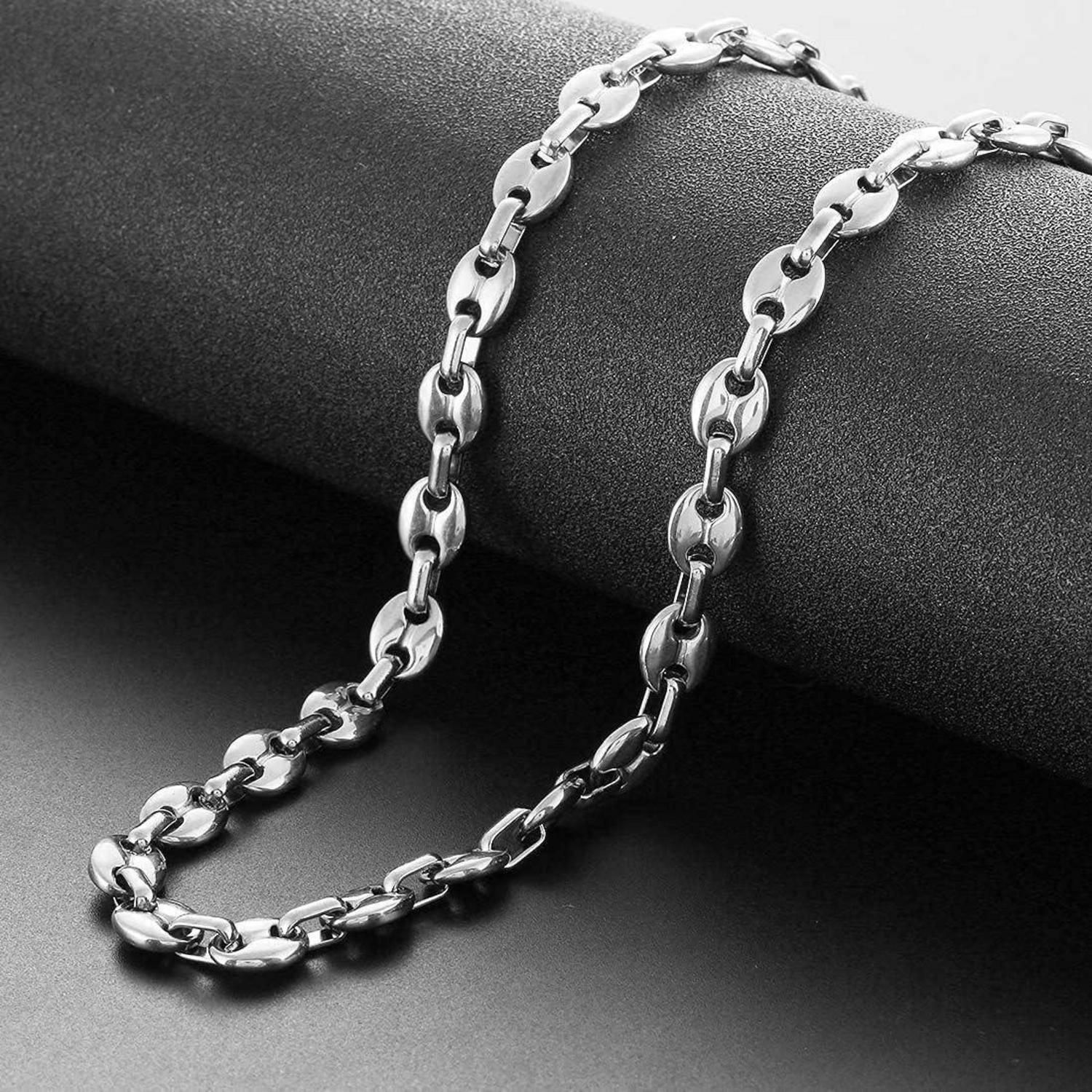 Eine Nahaufnahme einer glänzenden, silbernen Kette mit ineinandergreifenden ovalen Gliedern auf einer glatten, grauen Oberfläche. Die Kette ist in Form eines 'S' angeordnet.