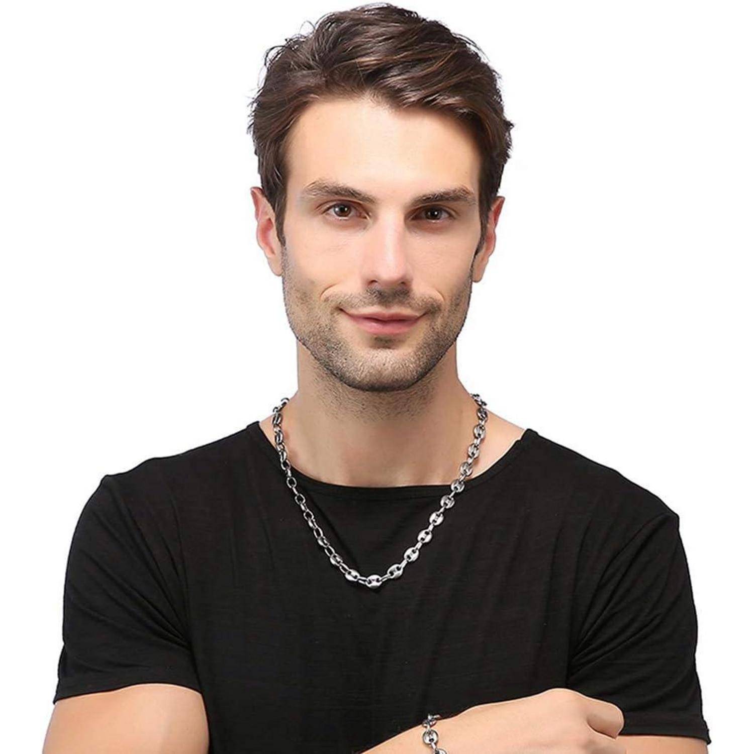 Mann in einem schwarzen T-Shirt und Halskette, lächelnd in die Kamera vor einem einfarbigen weißen Hintergrund.