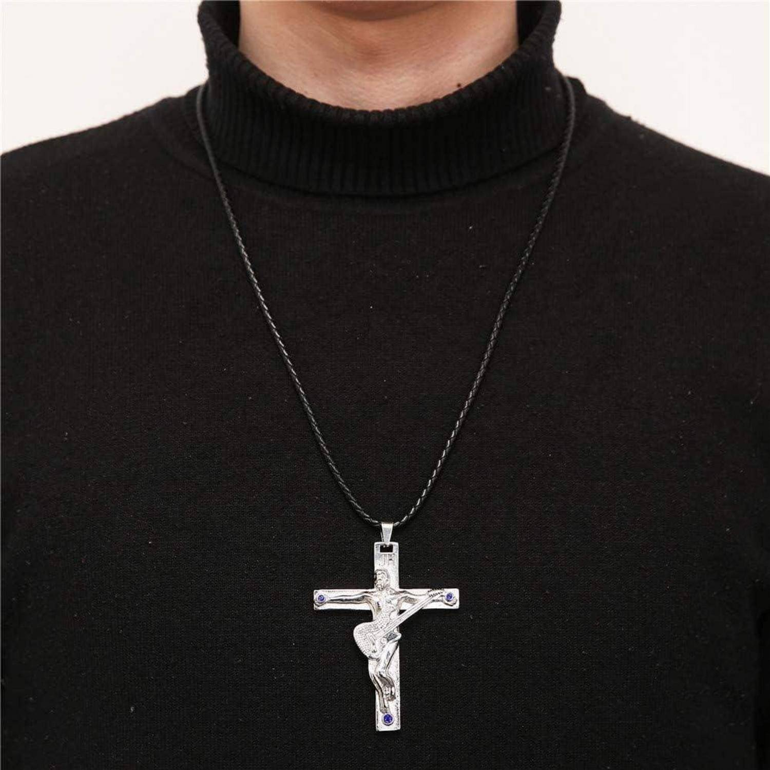 Eine Person, die einen schwarzen Rollkragenpullover trägt, mit einer silbernen Kreuzkette, die eine Figur von Jesus zeigt und kleine blaue Edelsteine an jeder Ecke besitzt.