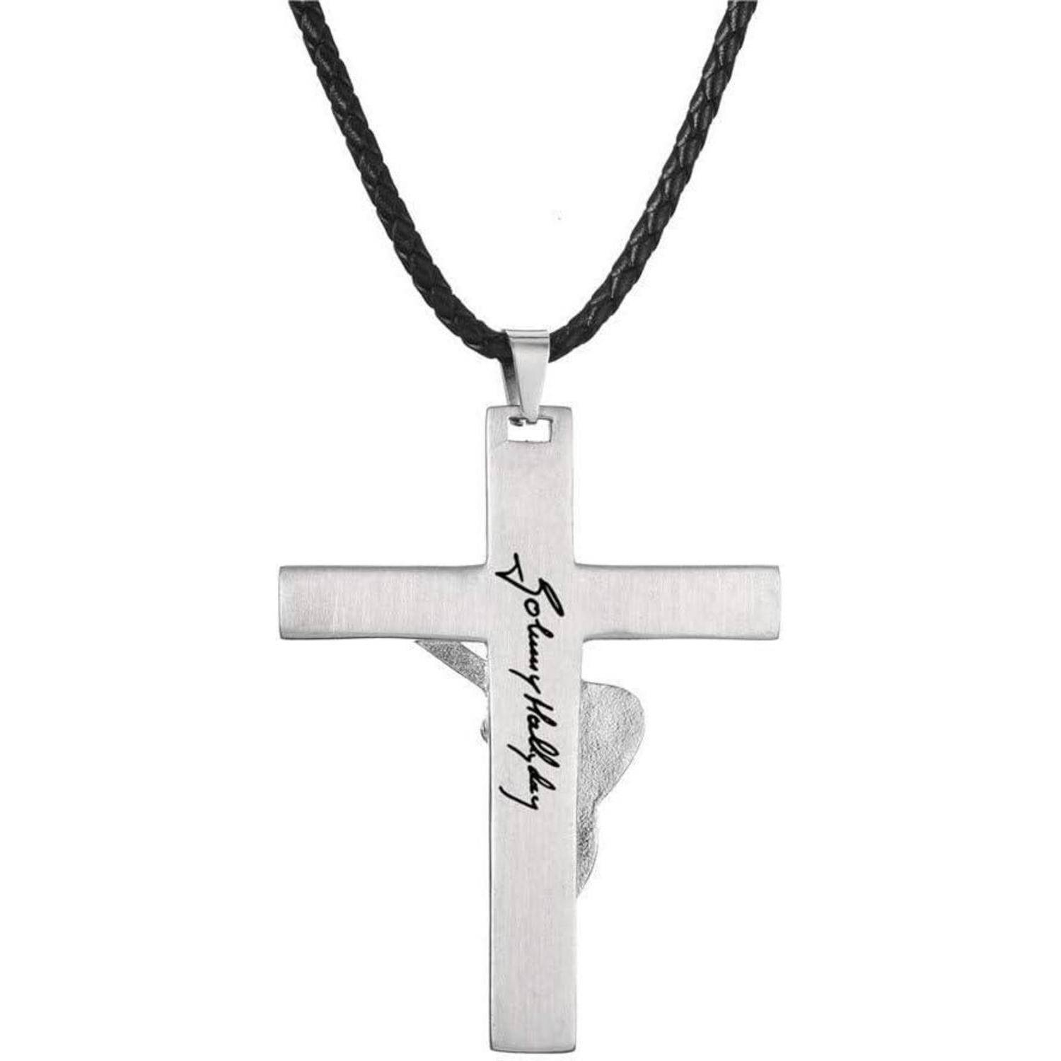 Ein silbernes Kreuz-Anhänger an einer schwarzen Schnur, mit einer gravierten Signatur auf der Vorderseite des Kreuzes.