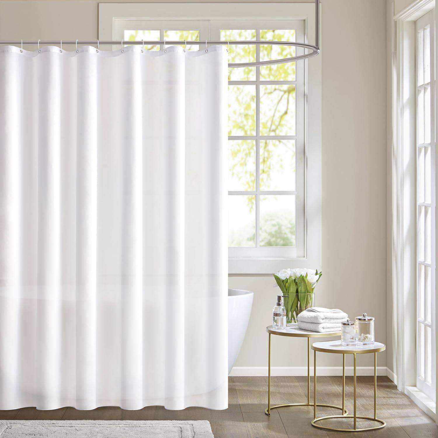 Helles Badezimmer mit einem großen Fenster, weißem Duschvorhang und minimaler Dekoration. Ein kleiner runder Tisch trägt ein Handtuch und Toilettenartikel.