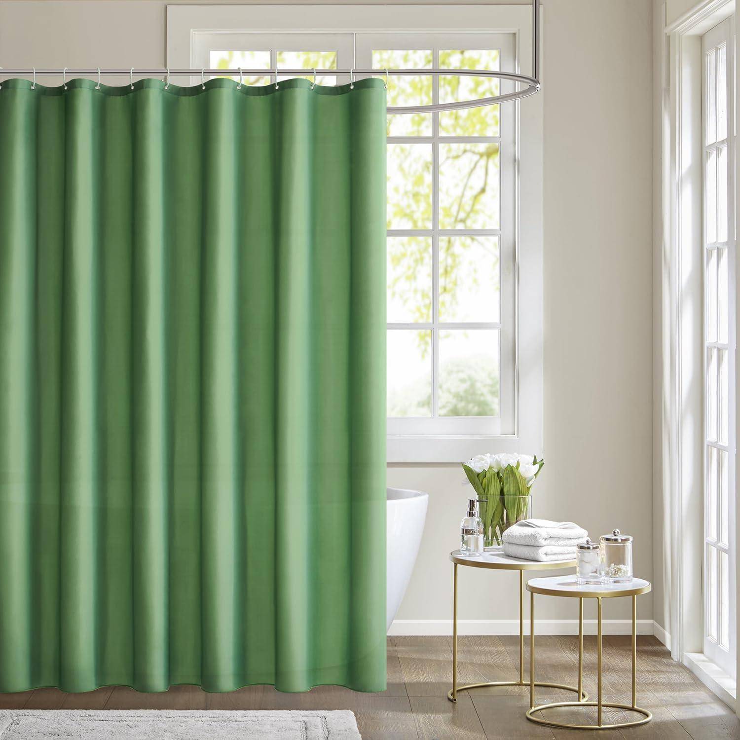 Grüner Duschvorhang, der in einem Badezimmer an einer weißen Badewanne hängt, mit einem Beistelltisch mit Handtüchern und einer Vase, und einem Fenster, das Grünpflanzen im Außenbereich zeigt.
