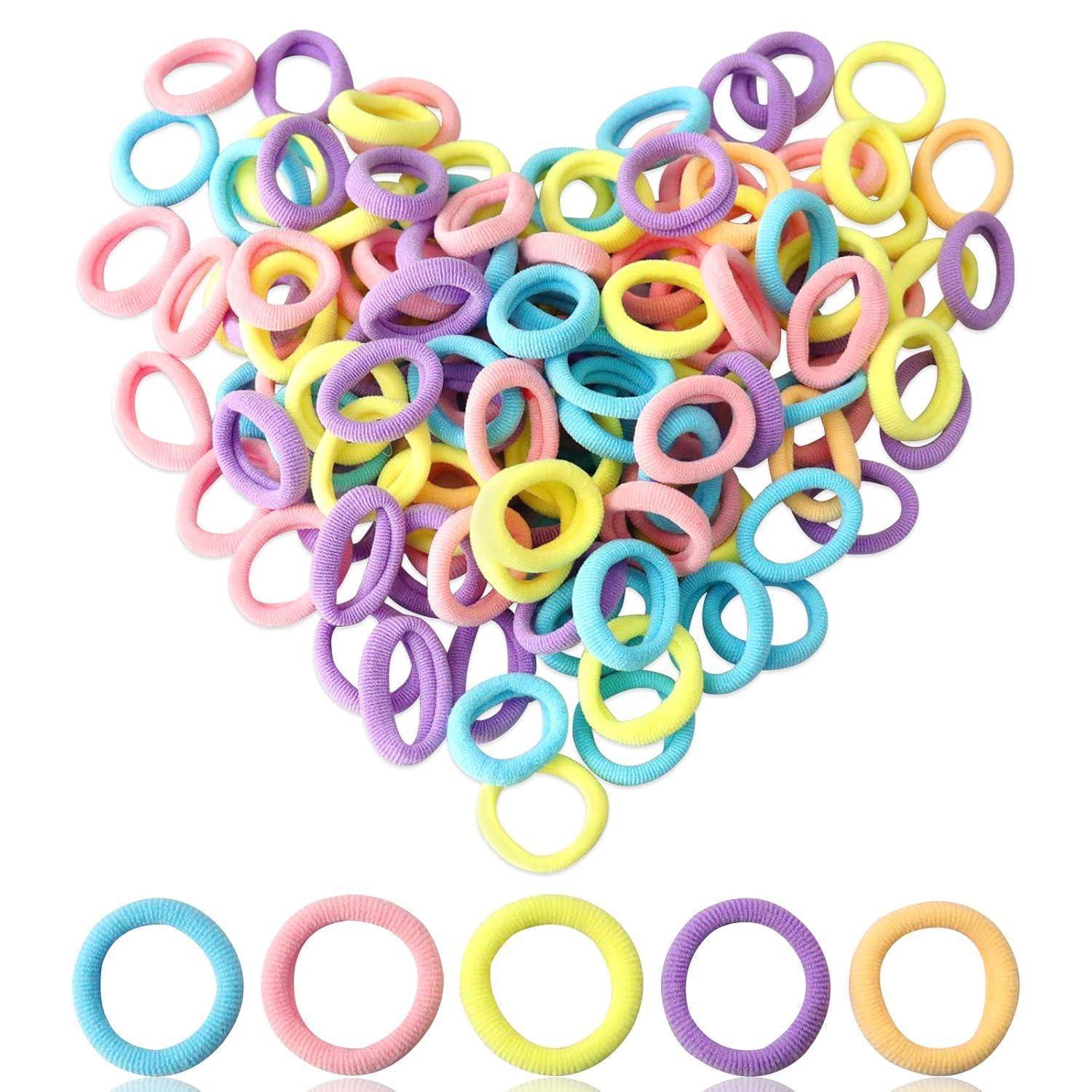 Ein herzförmiger Haufen bunter Haargummis in Rosa, Lila, Blau, Gelb und Grün. Fünf Haargummis in verschiedenen Farben sind darunter aufgereiht.