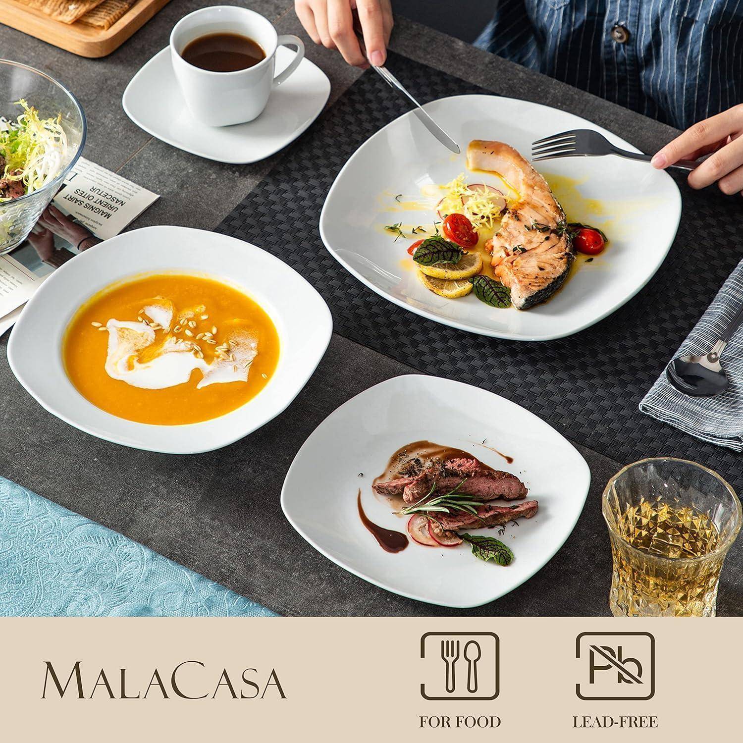 Ein Esstisch mit einer Mahlzeit, die Lachs, Suppe und Steak umfasst, gedeckt mit Tellern, Tassen und Besteck. Zwei Personen sitzen und essen gemeinsam.