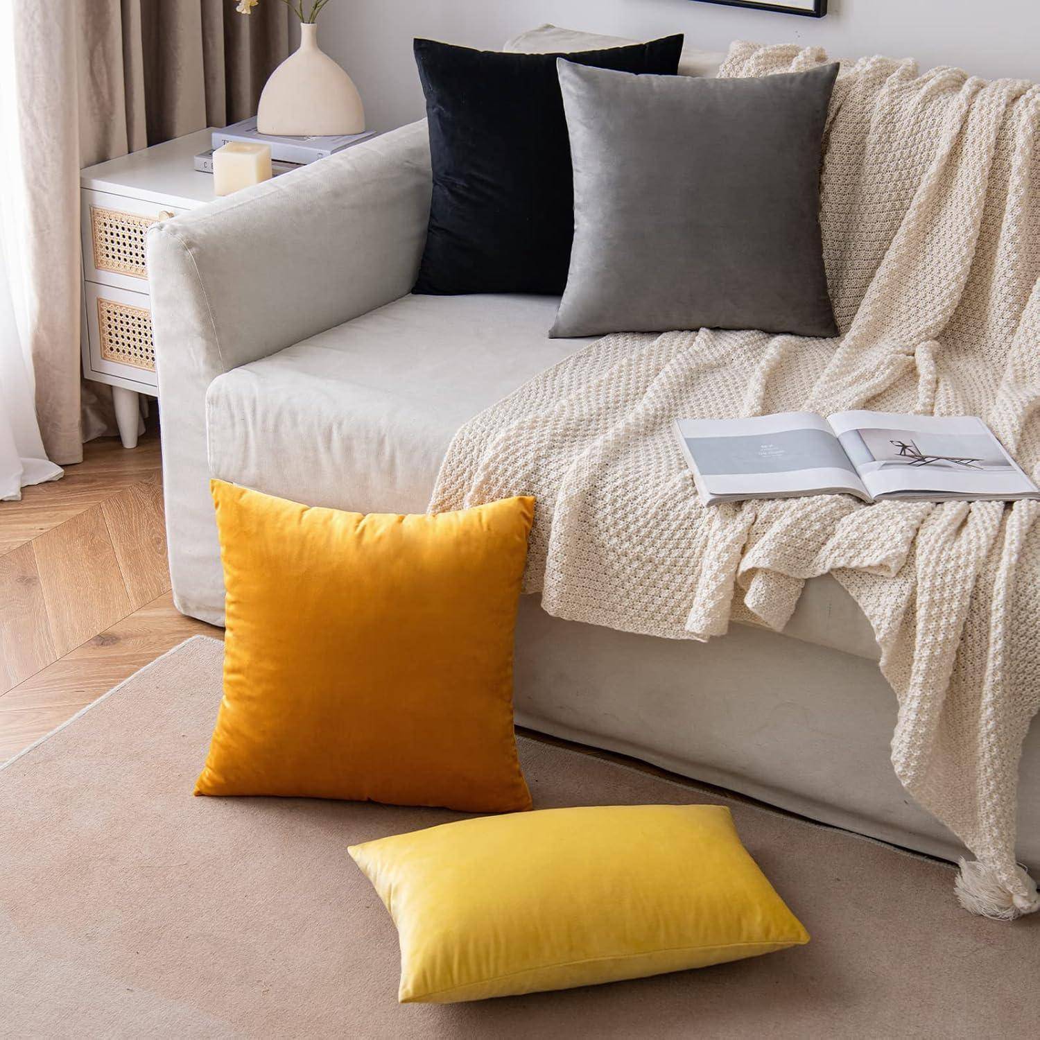 Ein gemütliches Wohnzimmer mit einem hellgrauen Sofa, darüber gebreitet eine Decke, verschiedene Kissen und ein aufgeschlagenes Buch, das auf dem Sofa liegt. Natürliches Licht fällt herein.