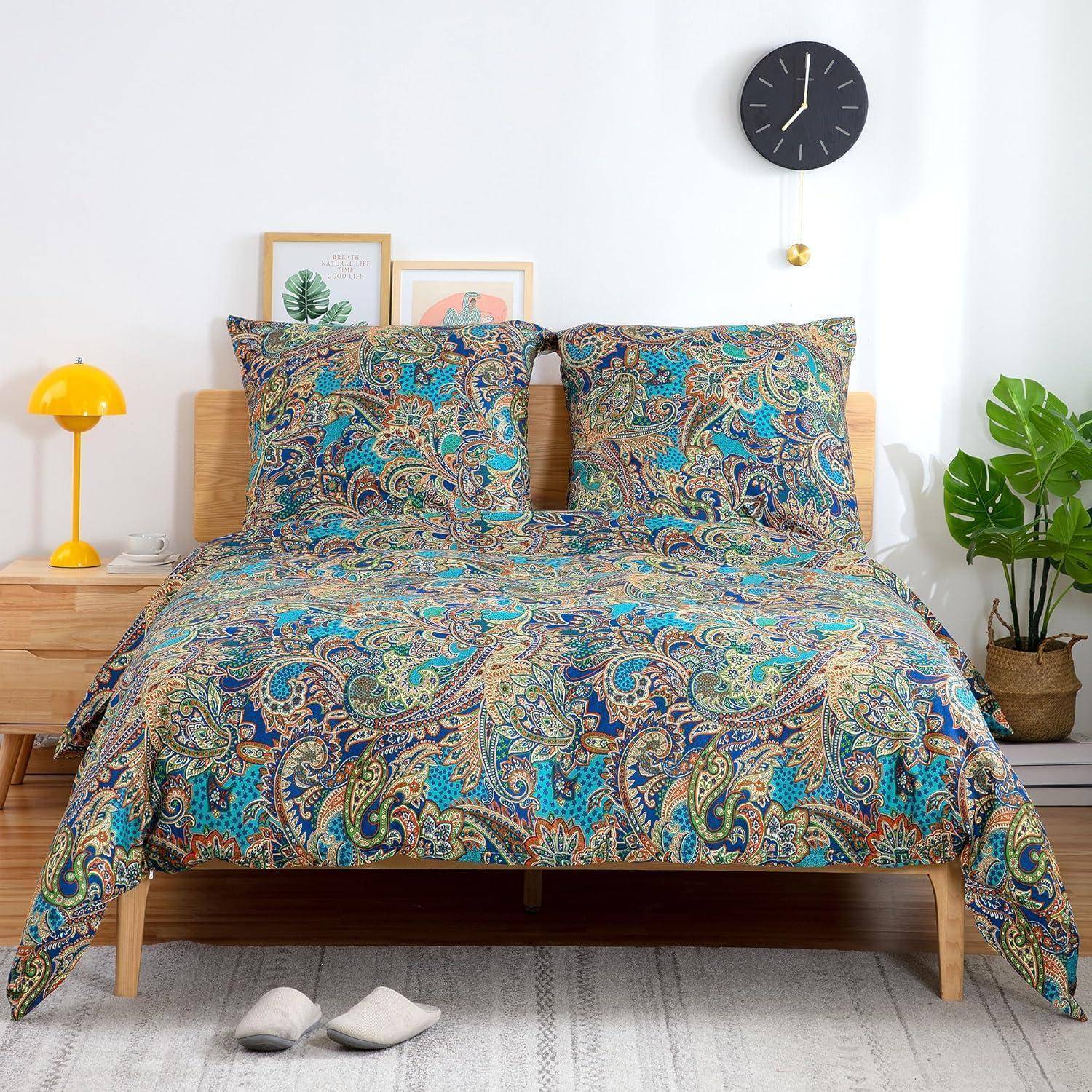 Ein Bett mit bunt gemusterter Paisley-Bettwäsche, zwei gerahmten Bildern am Holzkopfteil, einer gelben Lampe, einer Wanduhr und einer Zimmerpflanze.