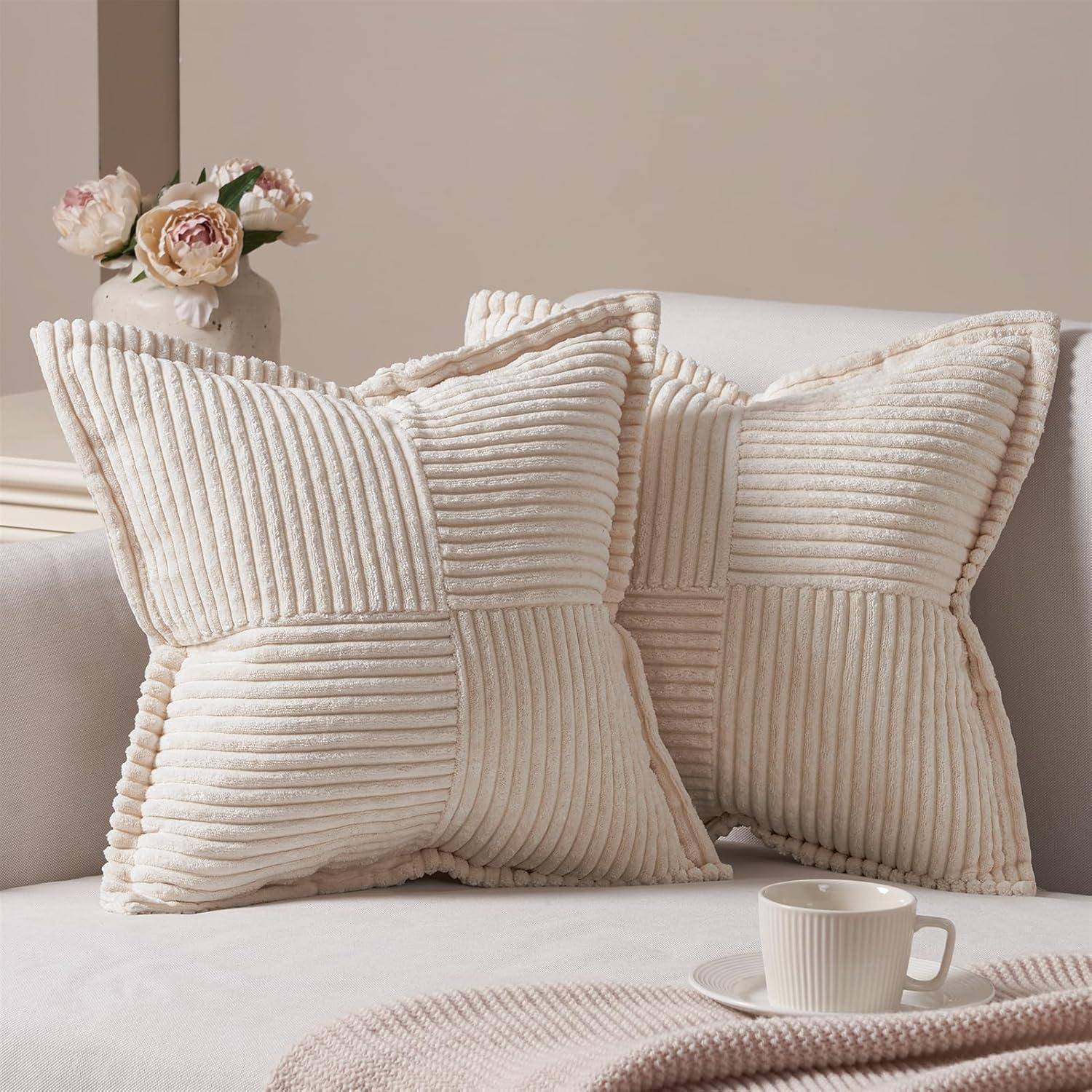 Zwei plüschige, strukturierte Kissen auf einem hellgefärbten Sofa, daneben eine Tasse mit Untertasse. Im Hintergrund befinden sich Blumen in einer Vase, die eine gemütliche Atmosphäre schaffen.