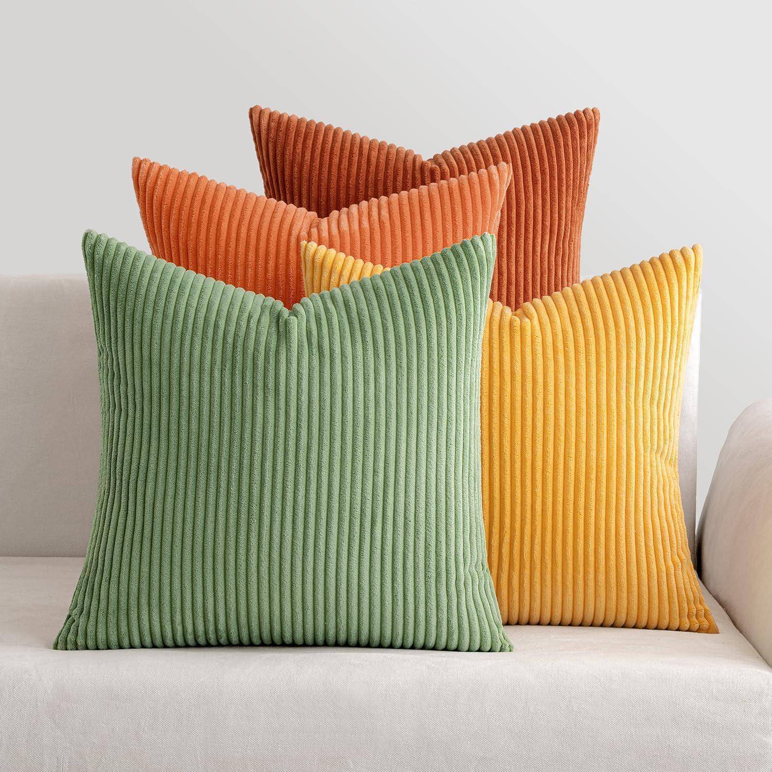 Drei gerippte Zierkissen in Grün, Orange und Gelb sind ordentlich auf einem weißen Sofa vor einer hellgrauen Wand angeordnet.