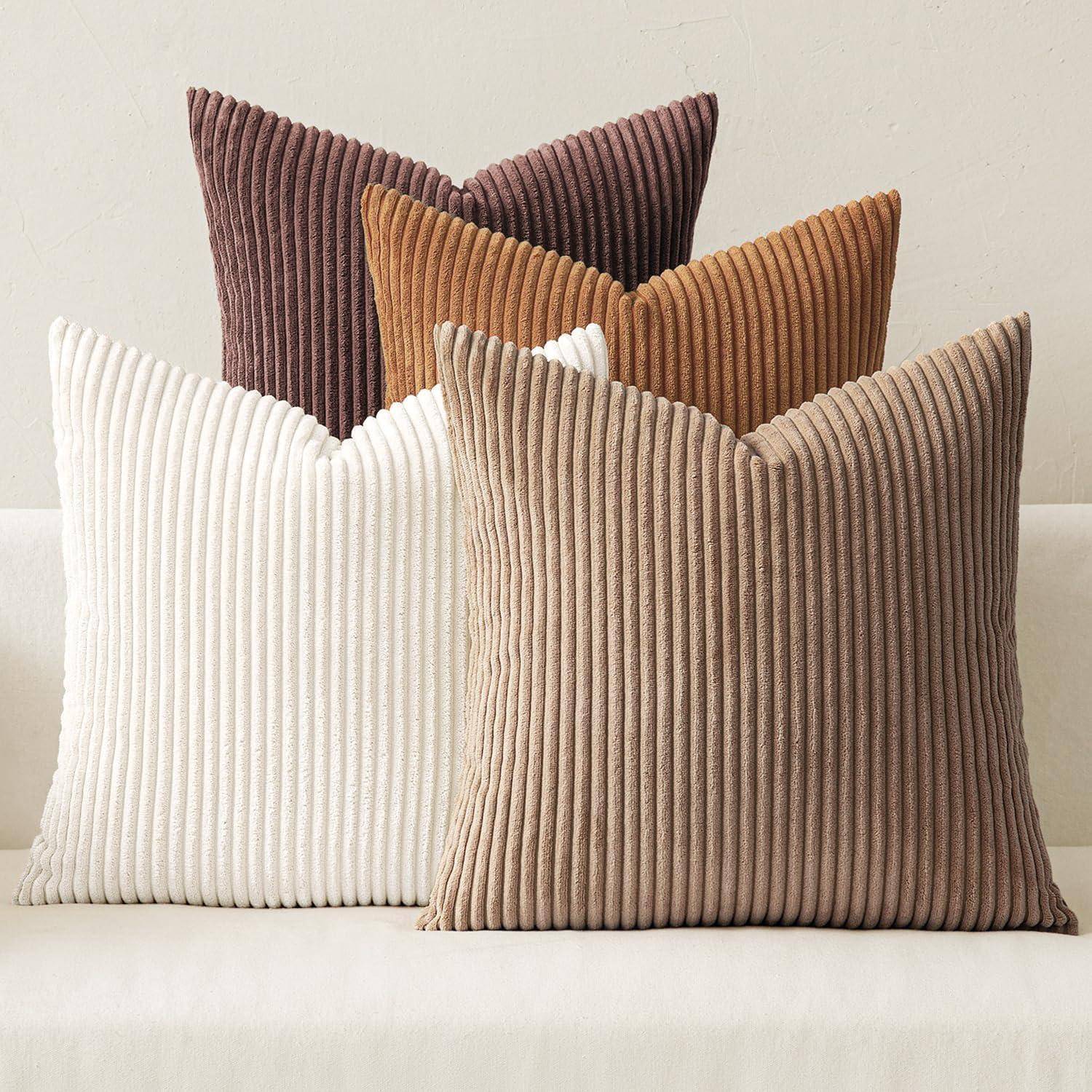 Vier gerippte Zierkissen in Beige, Weiß, Braun und Dunkelorange sind ordentlich auf einem hellgefärbten Sofa arrangiert.