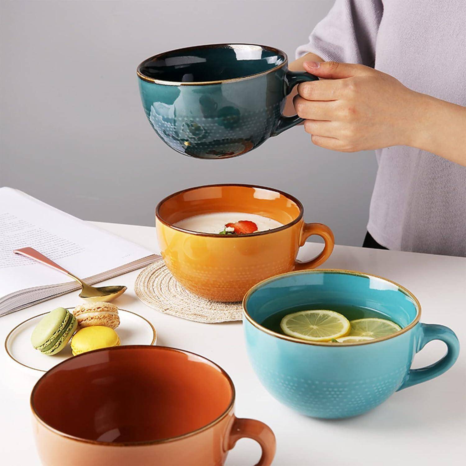 Eine Person gießt grünen Tee in eine türkisfarbene Tasse. In der Nähe sind ein aufgeschlagenes Buch, Macarons und andere Tassen auf einem weißen Tisch zu sehen.