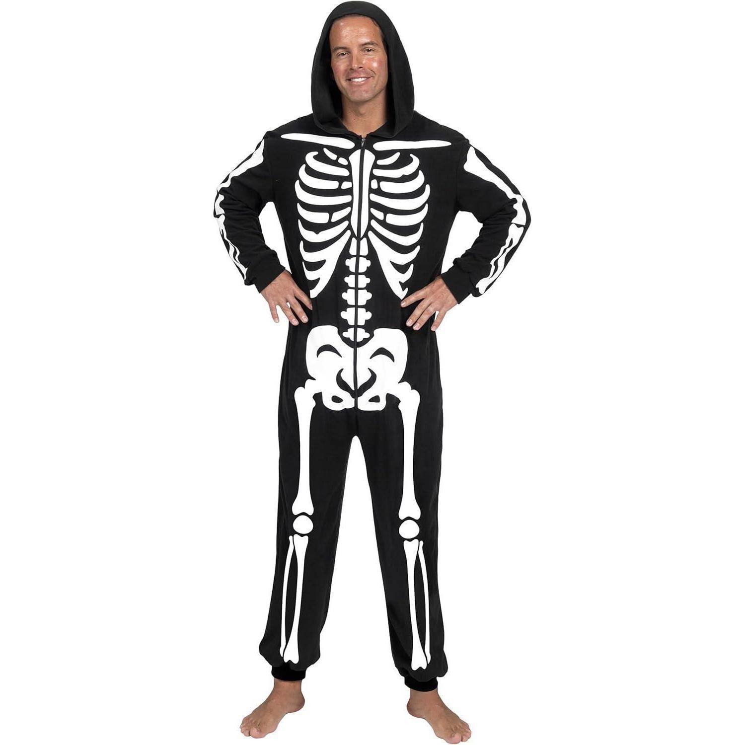 Mann in einem schwarzen Einteiler mit einem weißen Skelettdesign, barfuß auf einem einfarbigen Hintergrund stehend, lächelnd und die Hände in die Hüften gestemmt.