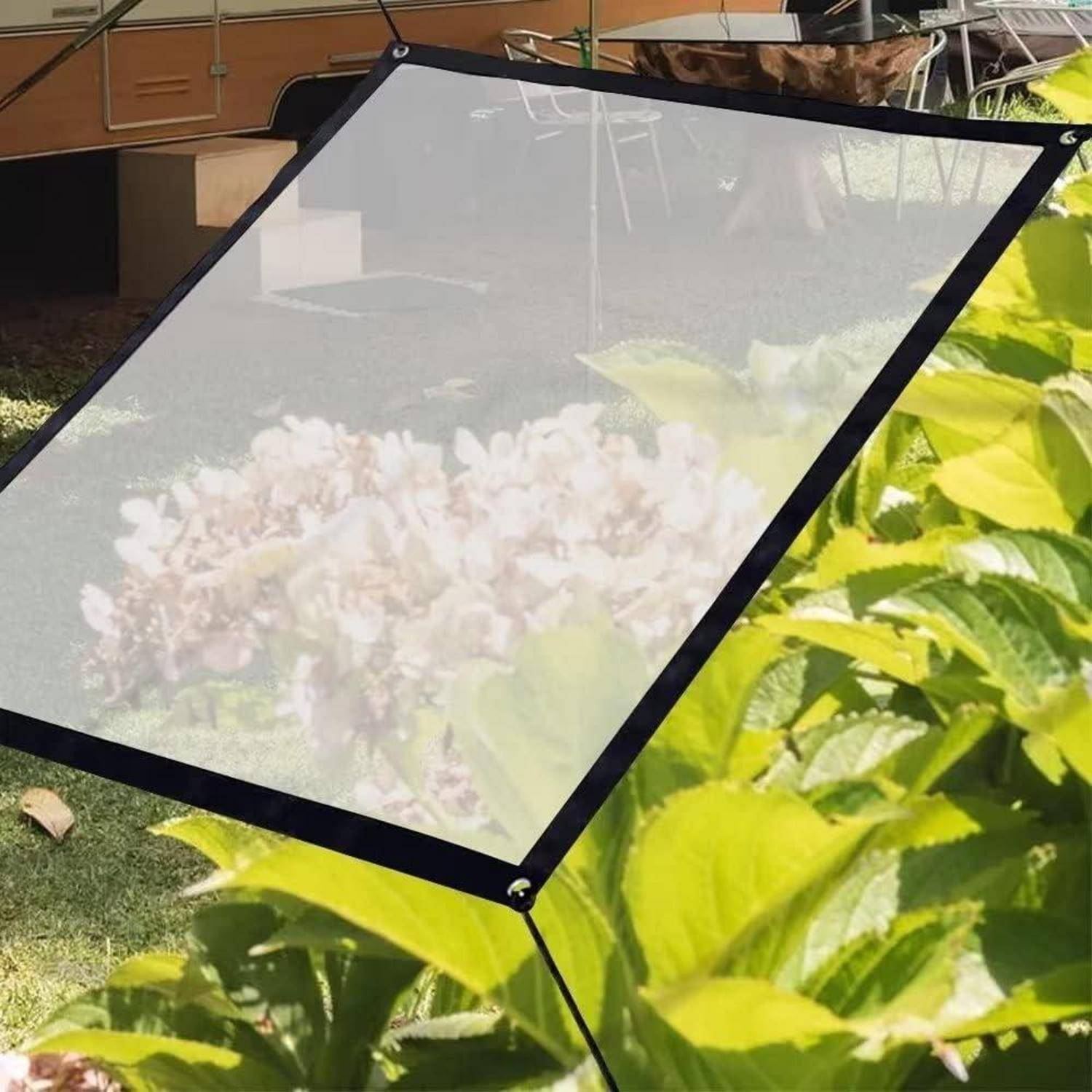 Eine mobile Outdoor-Projektionsleinwand steht auf einer grasigen Fläche mit blühenden Hortensien im Hintergrund. Ein Anhänger ist teilweise hinter der Leinwand sichtbar.