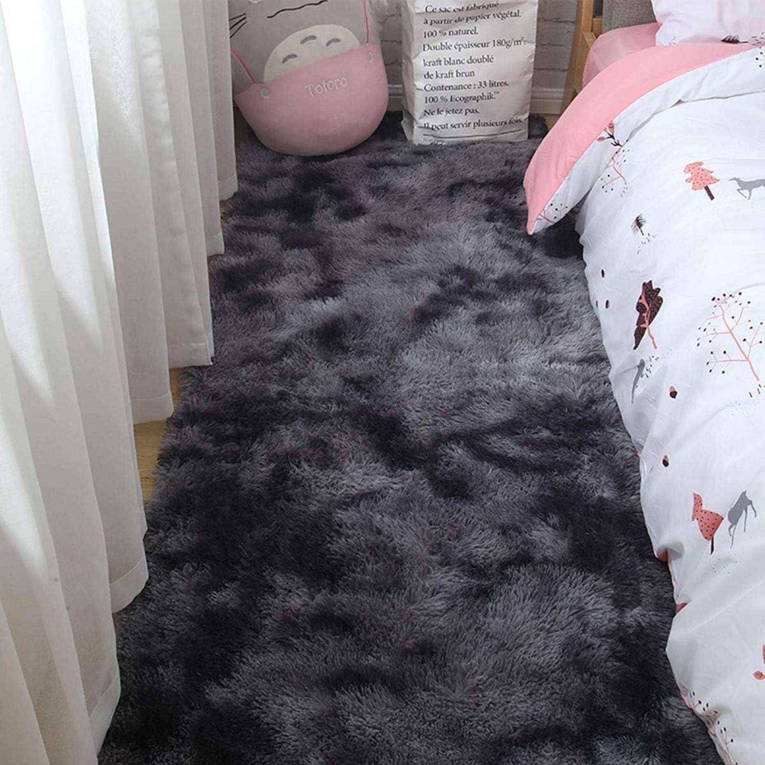 Eine Schlafzimmer-Szene mit einem flauschigen dunklen Teppich neben einem Bett, das mit einer weißen Bärchen-gemusterten Bettdecke bezogen ist. Ein großer Totoro-Plüsch ist in der Ecke sichtbar.