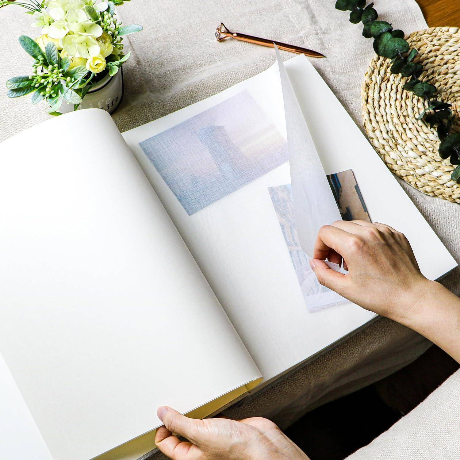 Eine Person schlägt eine Seite in einem Fotoalbum um und enthüllt verblasste Bilder. Ein Blumengesteck und ein geflochtenes Tischset befinden sich in der Nähe auf einem Holztisch.
