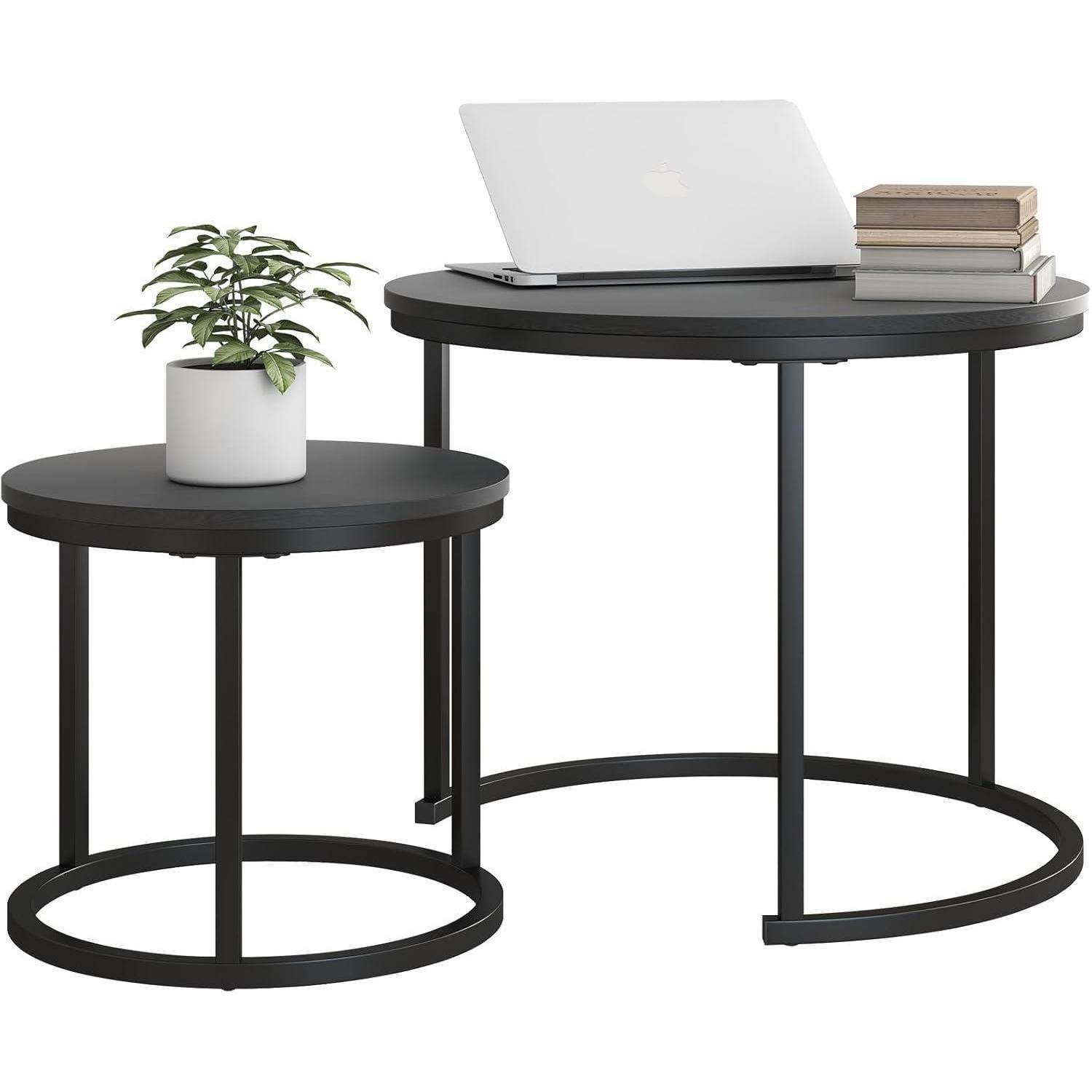 Zwei moderne runde Tische mit schwarzen Metallrahmen. Ein größerer Tisch trägt einen weißen Laptop und einen Stapel Bücher; auf einem kleineren Tisch steht eine Topfpflanze.
