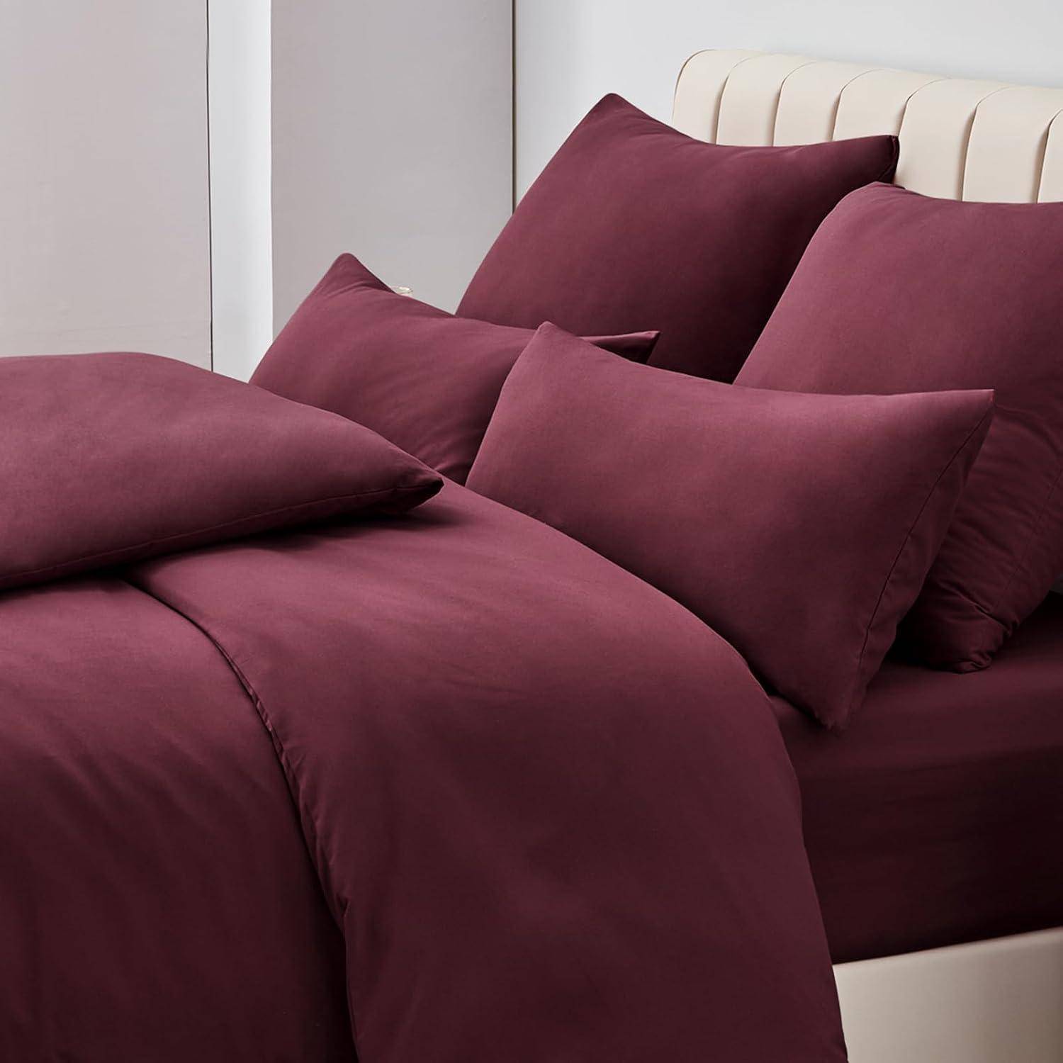 Ein Bett mit burgunderroten Laken, Kissen und einem Kopfteil in einer modernen Schlafzimmerumgebung, die die Textur und Farbe der Bettwäsche hervorhebt.