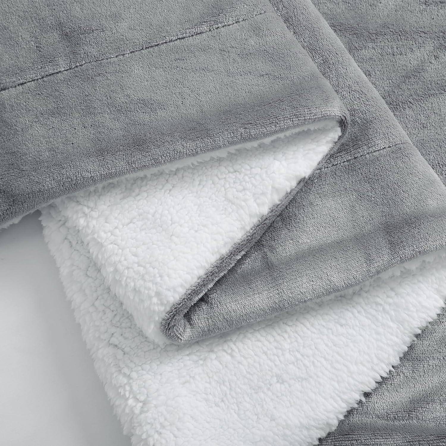 Eine gefaltete, weiche Fleece-Decke in Grau und Weiß mit sichtbaren Nähten, die ihre flauschige Textur hervorhebt, offensichtlich für Heimkomfort und Wärme.