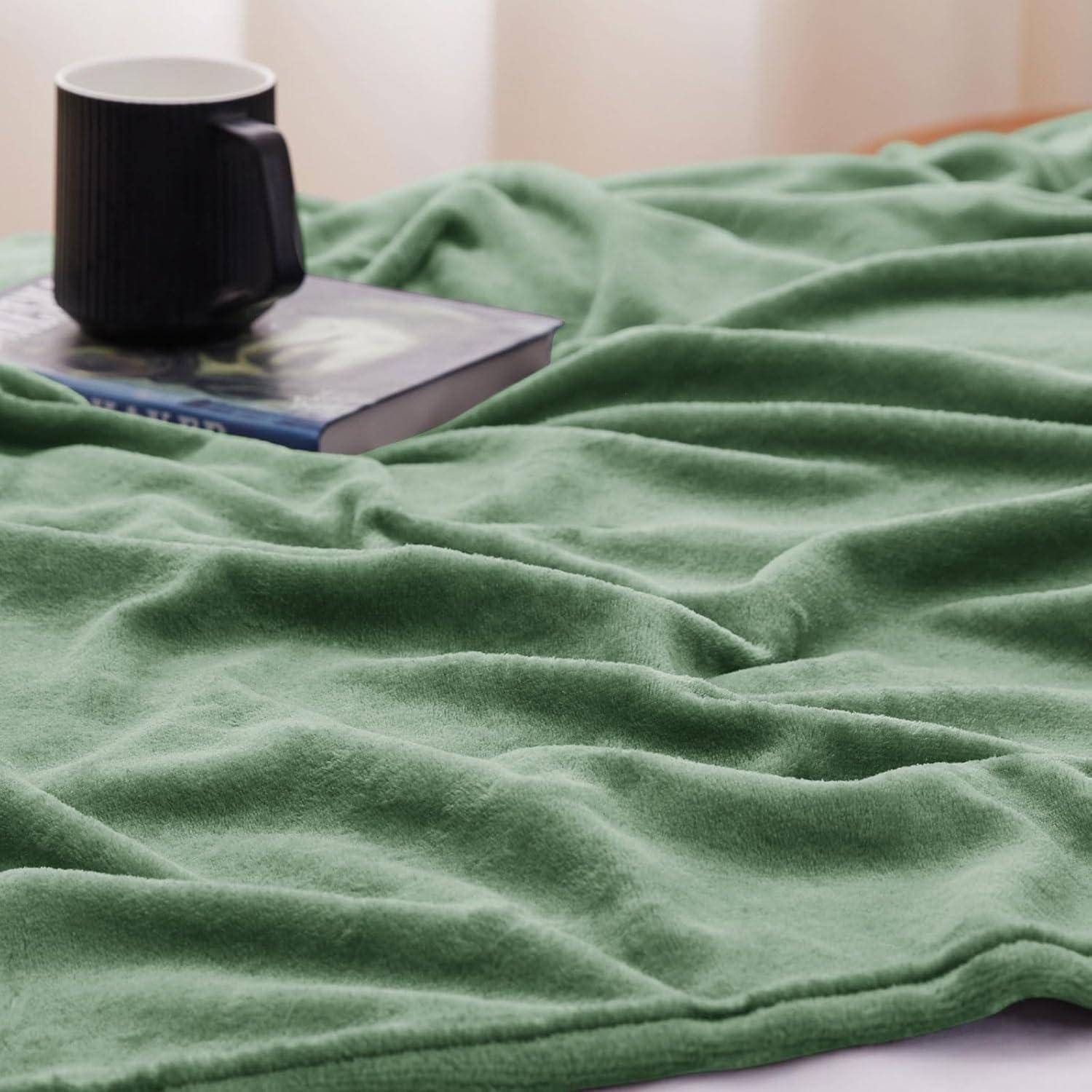 Eine grüne Decke ist auf einer Oberfläche neben einer schwarzen Tasse und einem Buch ausgebreitet und schafft eine gemütliche und einladende Atmosphäre.