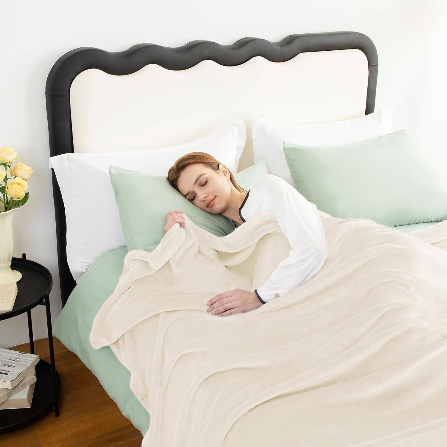 Eine Person, die friedlich in einem Bett mit weißen Laken und pastellfarbenen Kissen schläft. Ein Nachttisch mit einer Vase voller Blumen und Bücher steht in der Nähe.