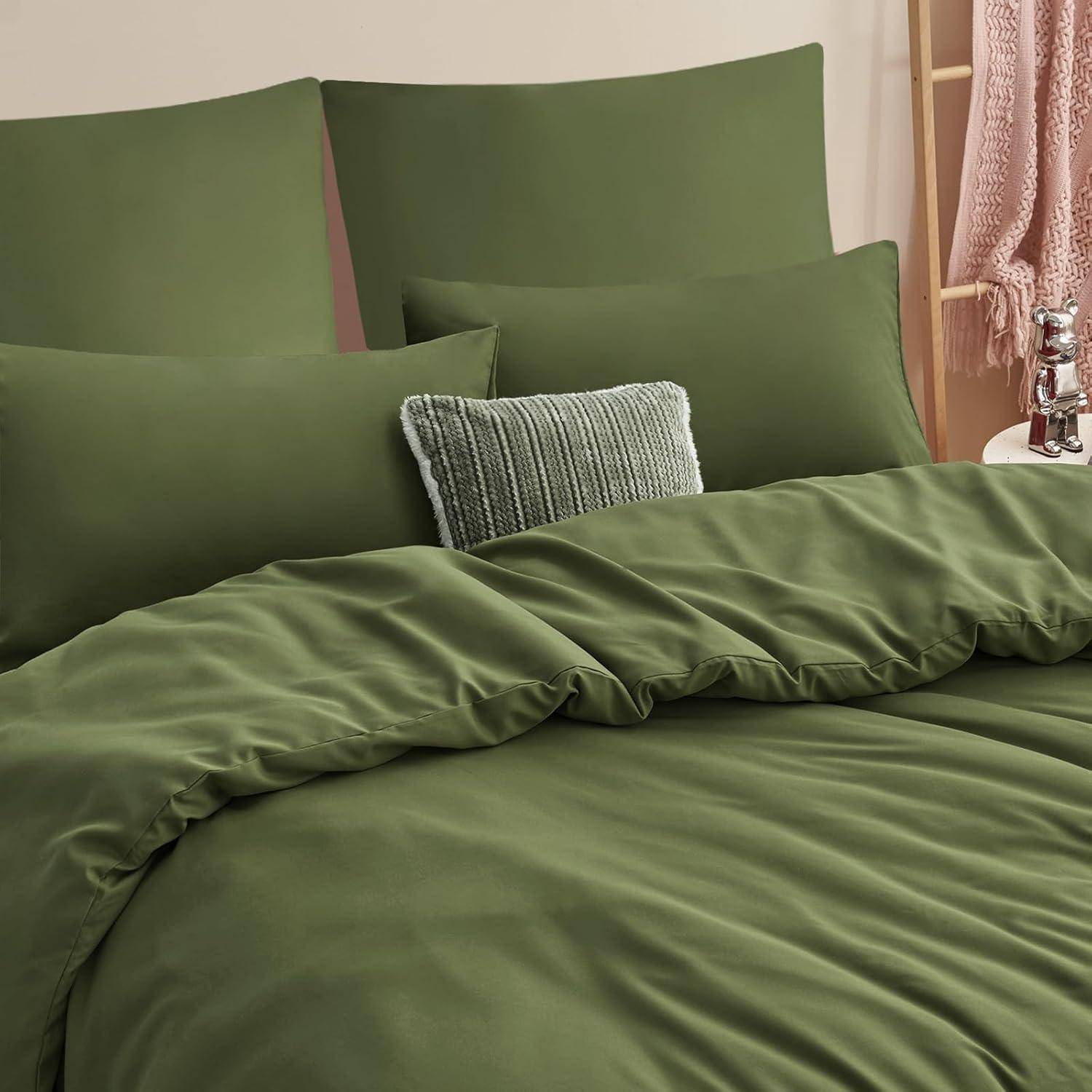 Ein Schlafzimmer zeigt ein ordentlich gemachtes Bett mit olivgrüner Bettwäsche und Kissen. Ein strukturiertes Kissen befindet sich in der Mitte und schafft einen Kontrast.