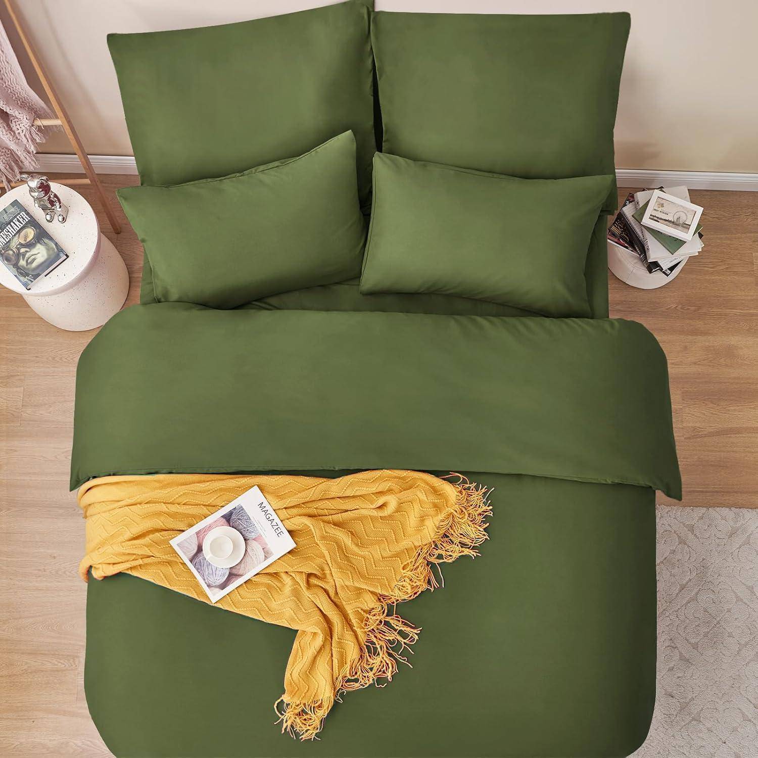 Ein sorgfältig aufgemachtes Bett mit grüner Bettwäsche und einer orangefarbenen Decke. Zwei grüne Kissen sind aufgestellt, und in der Nähe auf dem Boden liegen Bücher.