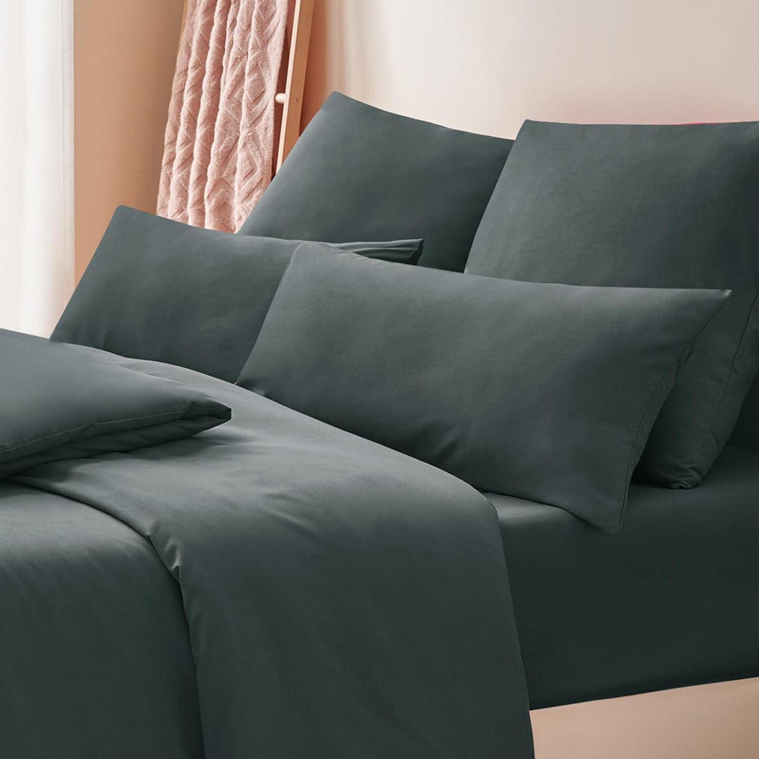 Ein ordentlich gemachtes Bett mit dunkeltürkisfarbenen Bettwäsche und Kissenbezügen vor einer beigen Wand, mit strukturierten beigen Vorhängen.