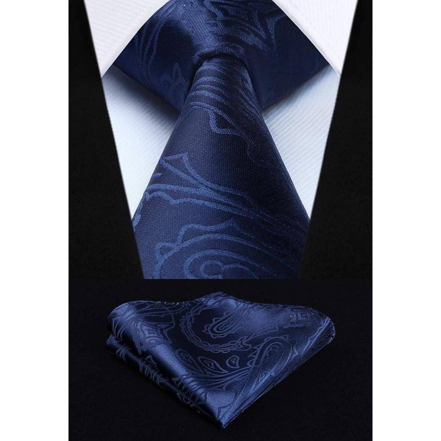 Eine marineblau-farbene Krawatte mit einem dezenten Paisley-Muster ist ordentlich um den Kragen eines weißen Hemdes gebunden. Darunter ist ein gefaltetes Einstecktuch mit dem gleichen Design platziert.