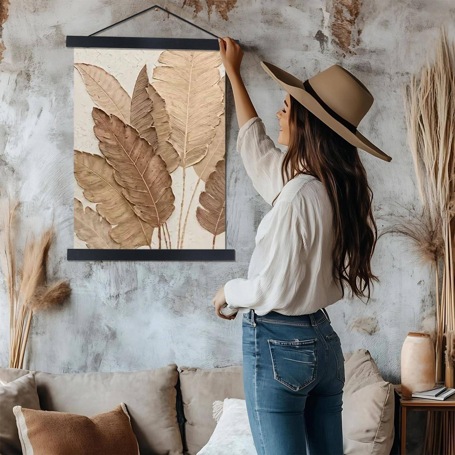 Eine Frau mit einem breiten Hut betrachtet ein gerahmtes botanisches Kunstwerk an einer strukturierten Wand und steht in einem stilvollen Wohnzimmer mit einem Sofa.